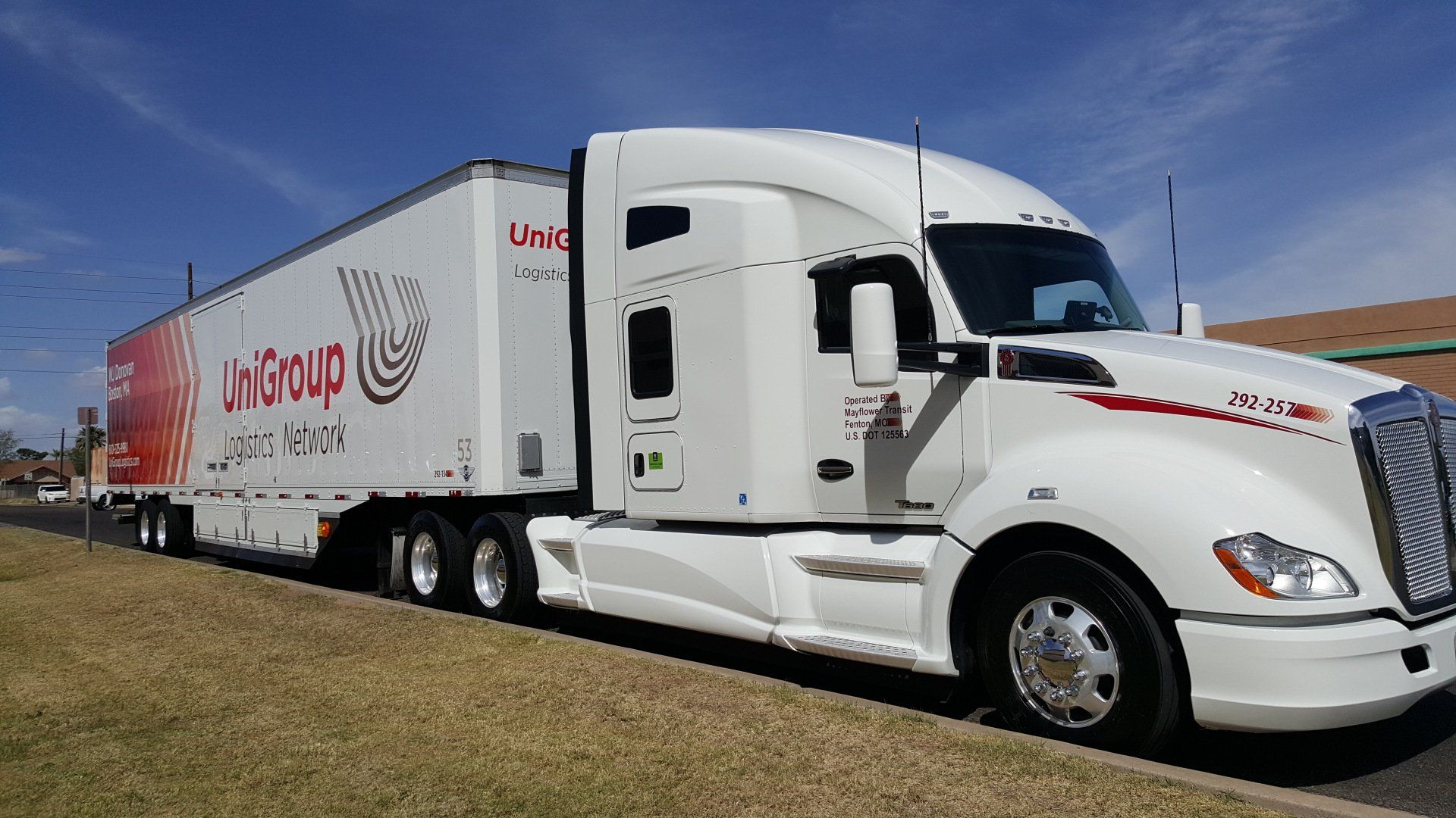 White semi-truck with a refrigerated trailer parked on grass under a blue sky.