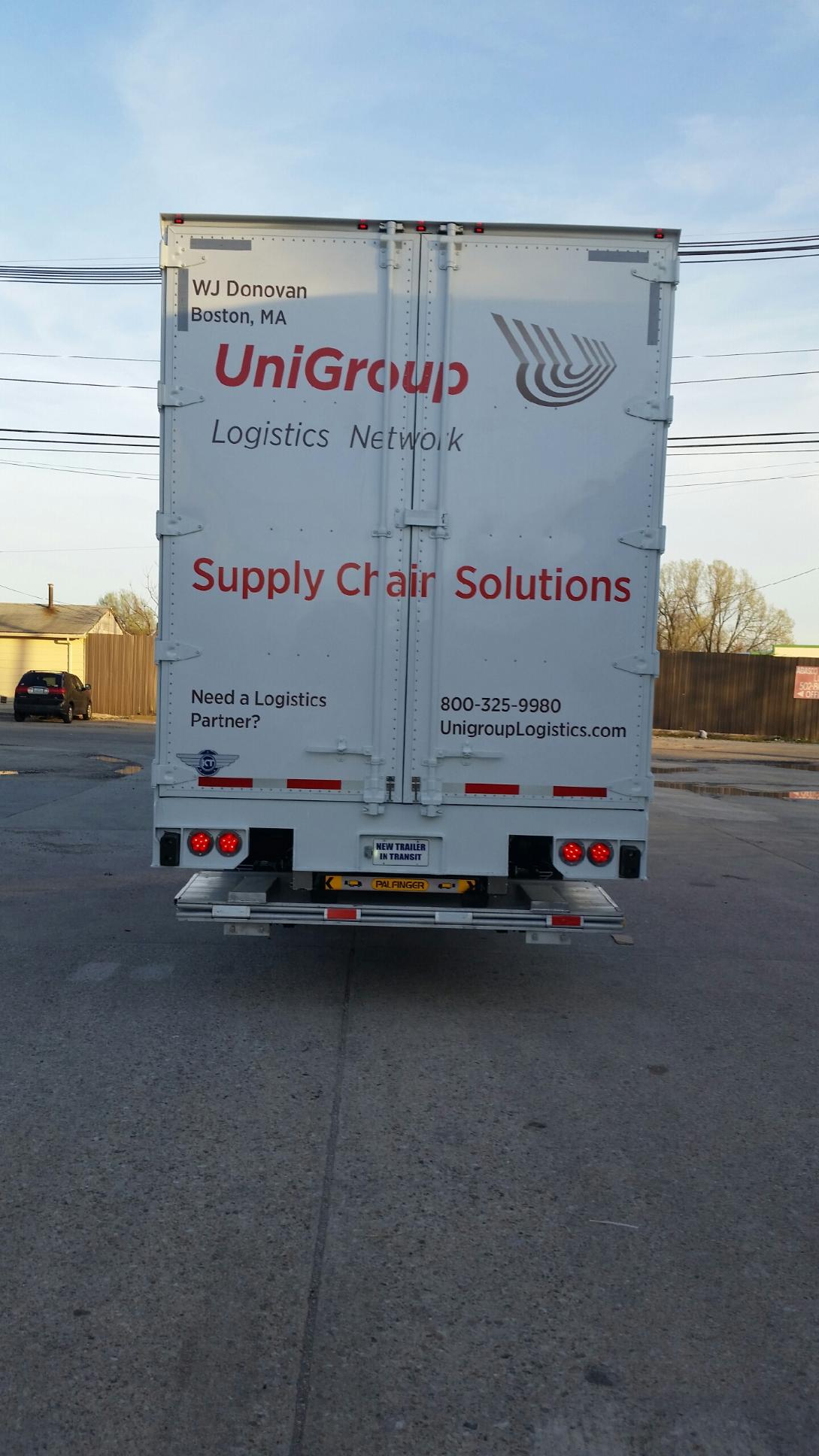 Rear view of a white UniGroup Supply Chain Solutions truck parked on a road under a blue sky.