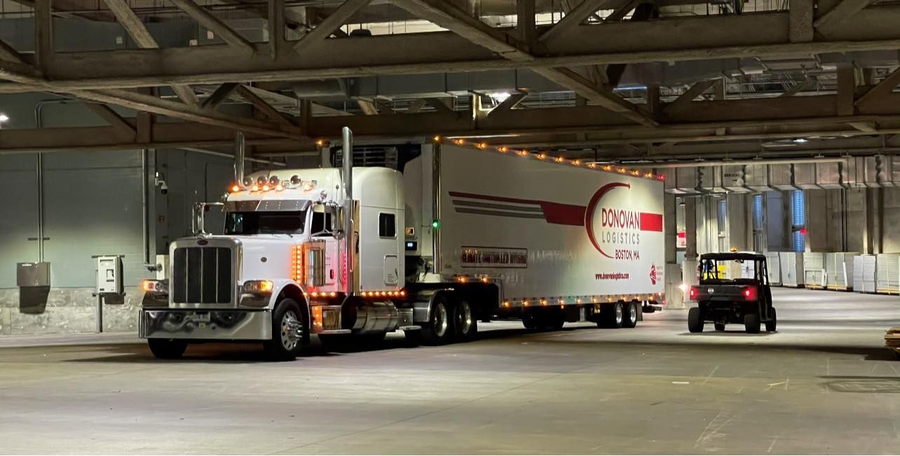 Semi truck and trailer parked in an indoor loading dock, with a small utility vehicle nearby.