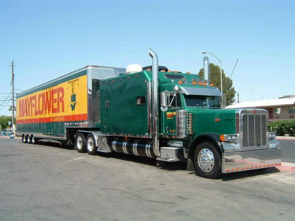 Green semi-truck hauling a yellow trailer with red lettering on a sunny street