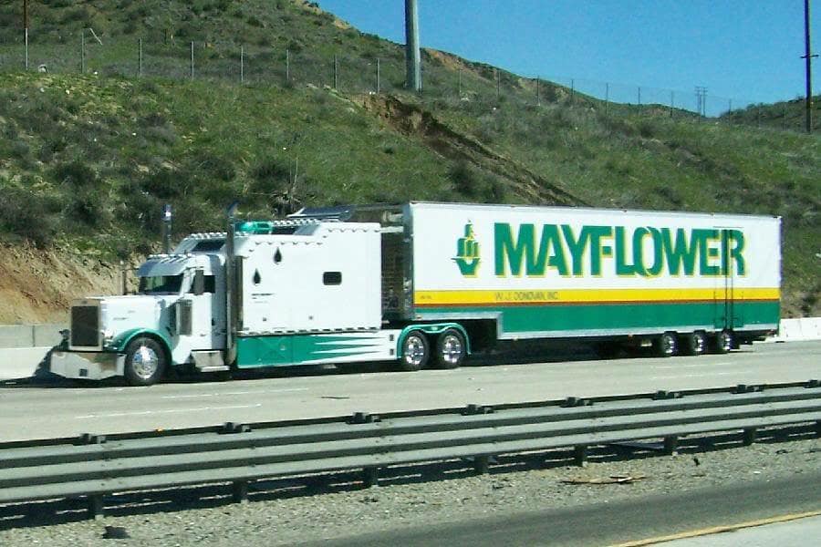 White Mayflower moving truck on a highway beside a grassy hillside