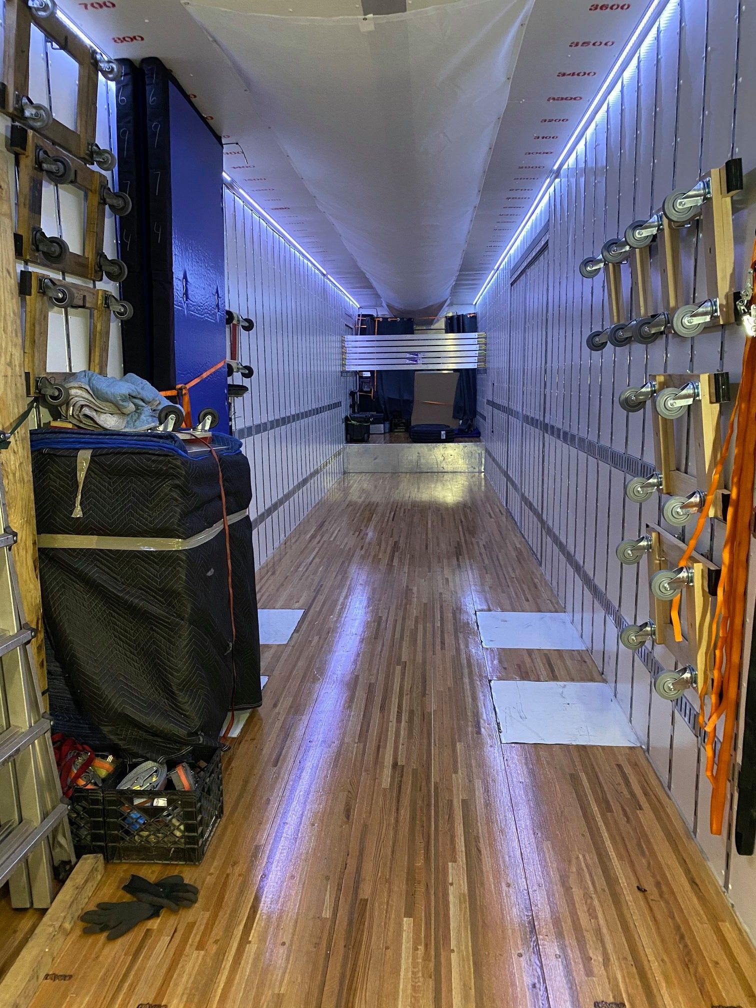 Interior of a cargo truck with wooden floor, shelves, and equipment along both sides of a narrow aisle.
