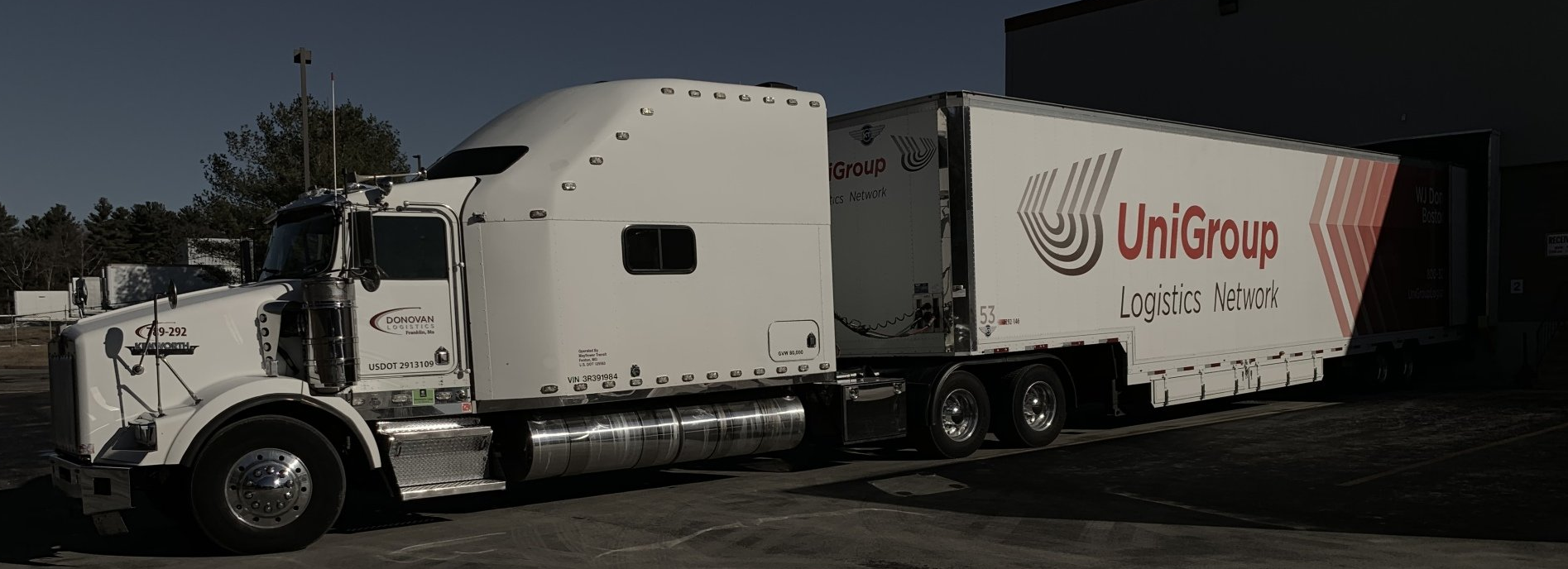 White semi-truck and trailer with UniGroup logo parked on a street in daylight