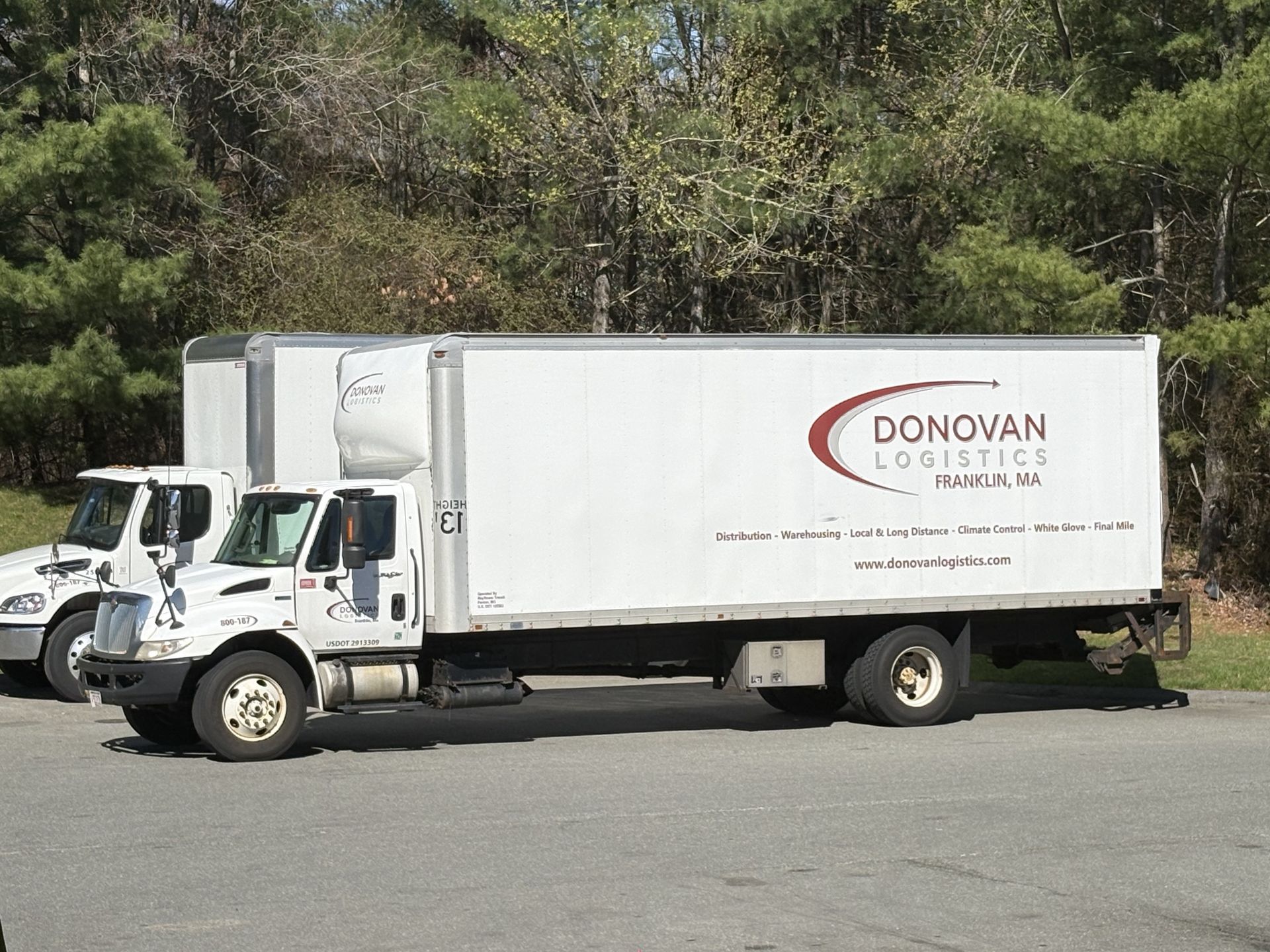 White Donovan Logistics box truck parked on pavement with trees in the background