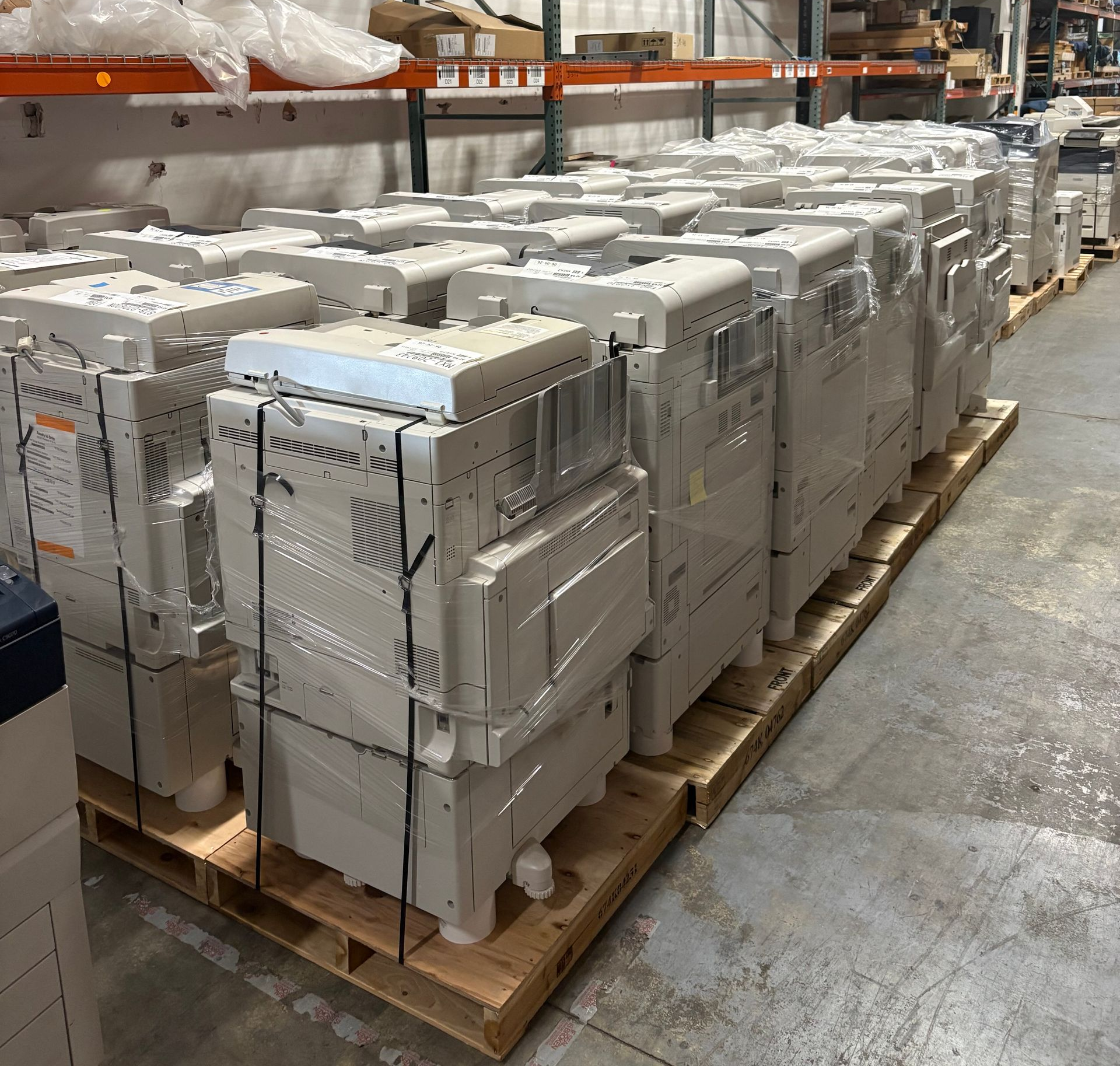 Pallets stacked with wrapped gray appliances in a warehouse aisle, ready for shipping.