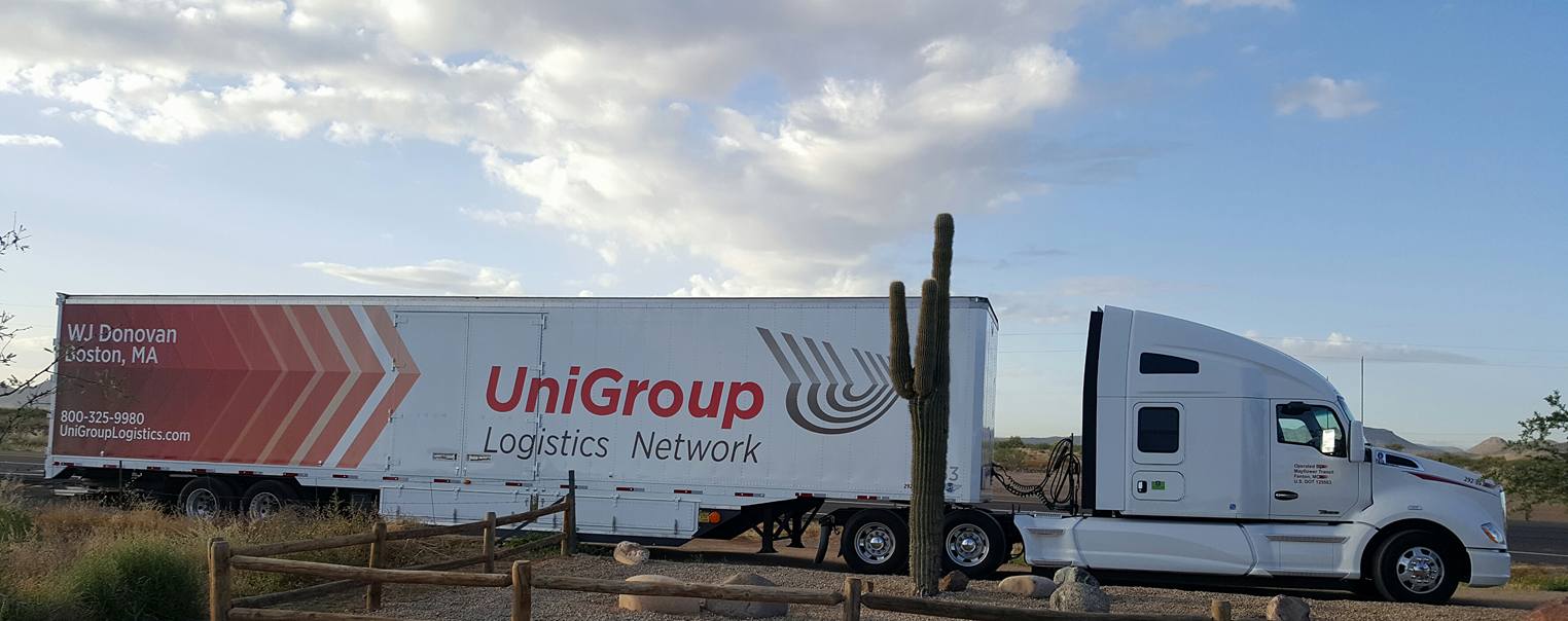 White UniGroup moving truck driving on a road under a cloudy sky