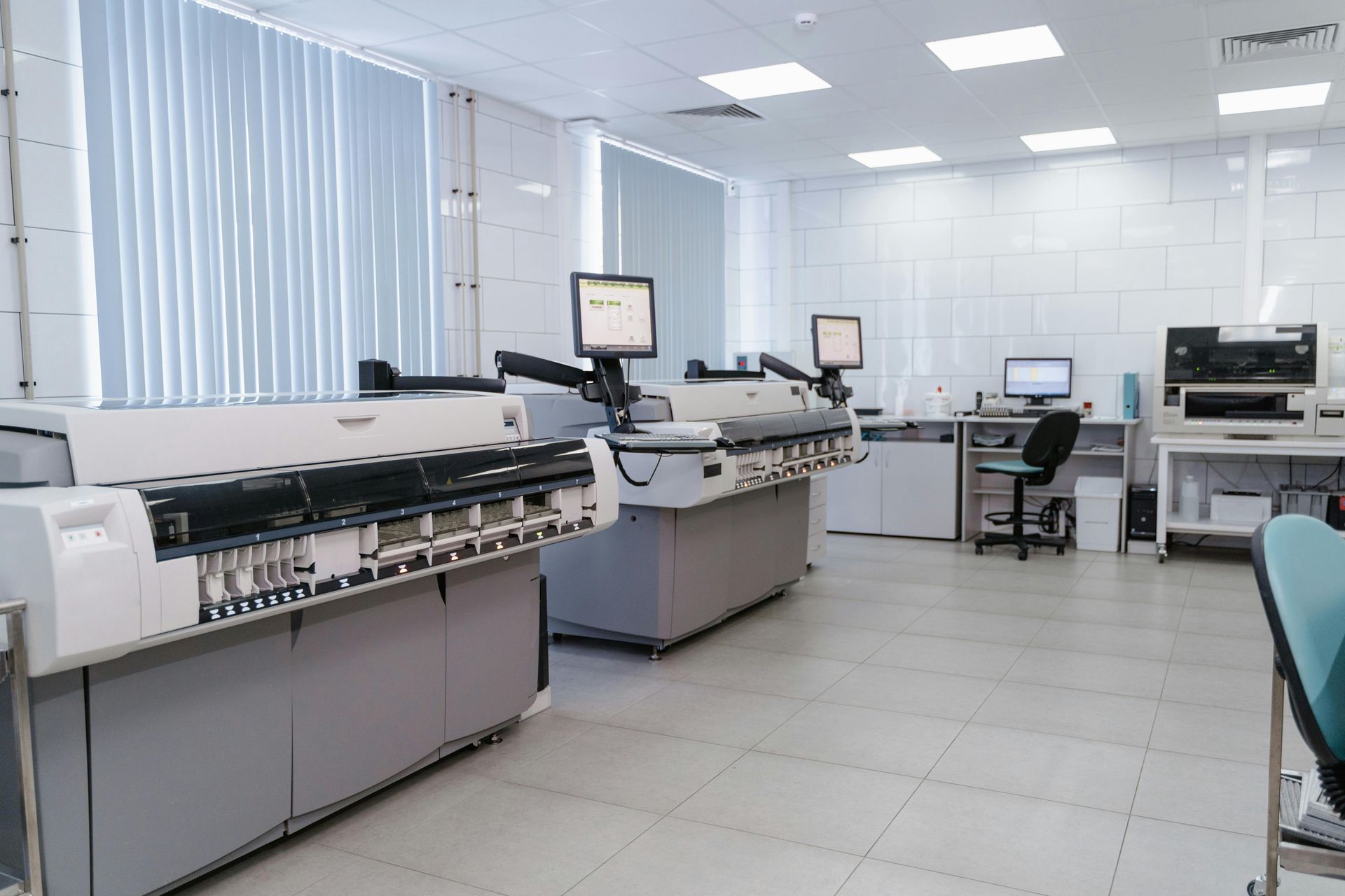 Bright laboratory room with automated medical equipment, monitors, and white tile walls