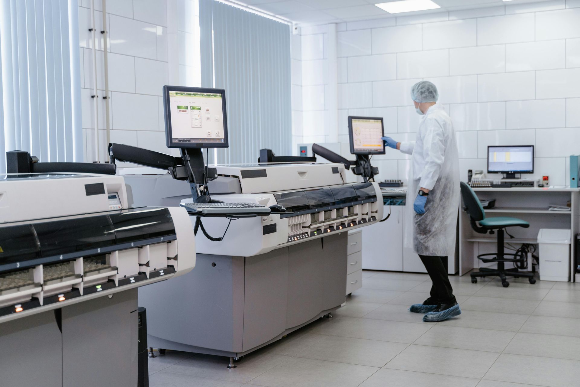 Laboratory technician in a white cleanroom operating automated lab equipment with computer monitors