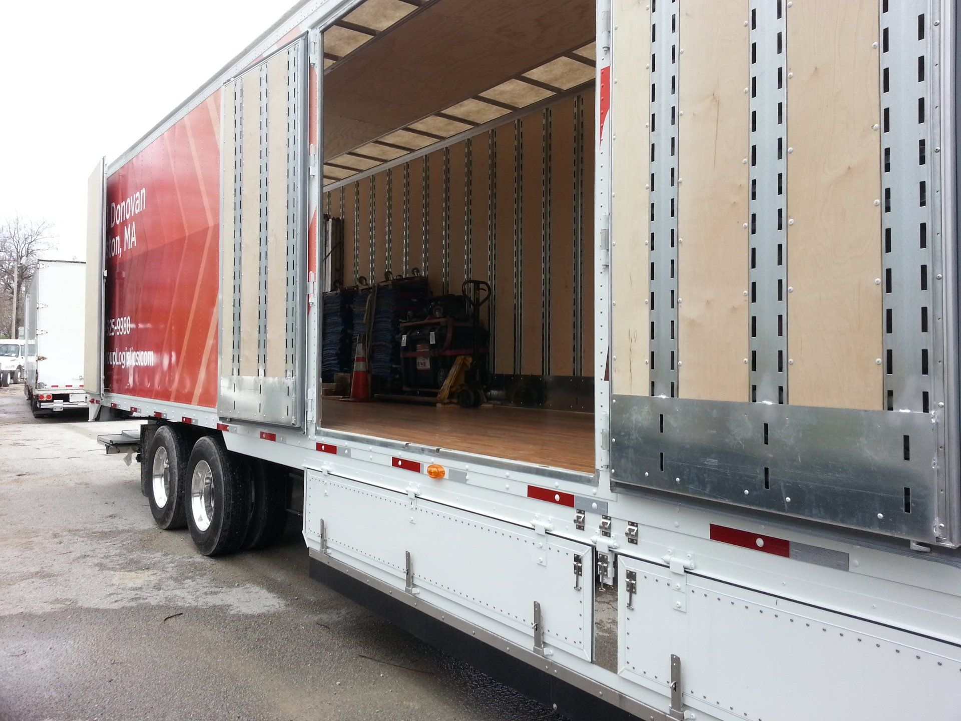 Open semi-trailer with cargo area exposed, parked on a wet street