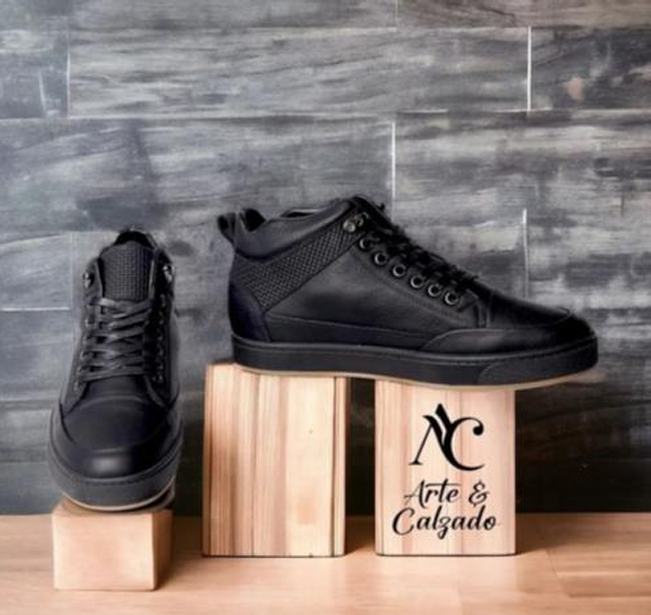 Un par de zapatillas deportivas negras de caña alta expuestas sobre bloques de madera frente a un muro de piedra gris