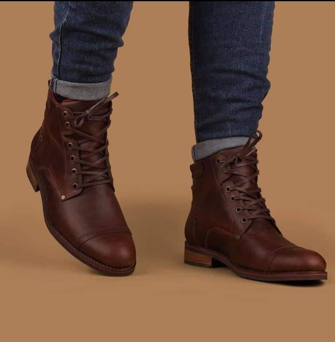 Botas marrones de cuero con cordones, combinadas con vaqueros azules remangados sobre un fondo marrón liso.