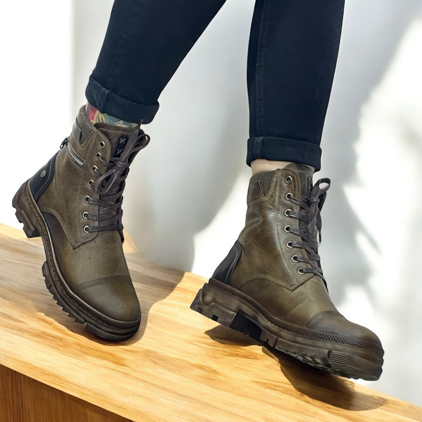 Una persona lleva puestas unas botas de cuero verde oscuro con cordones mientras camina