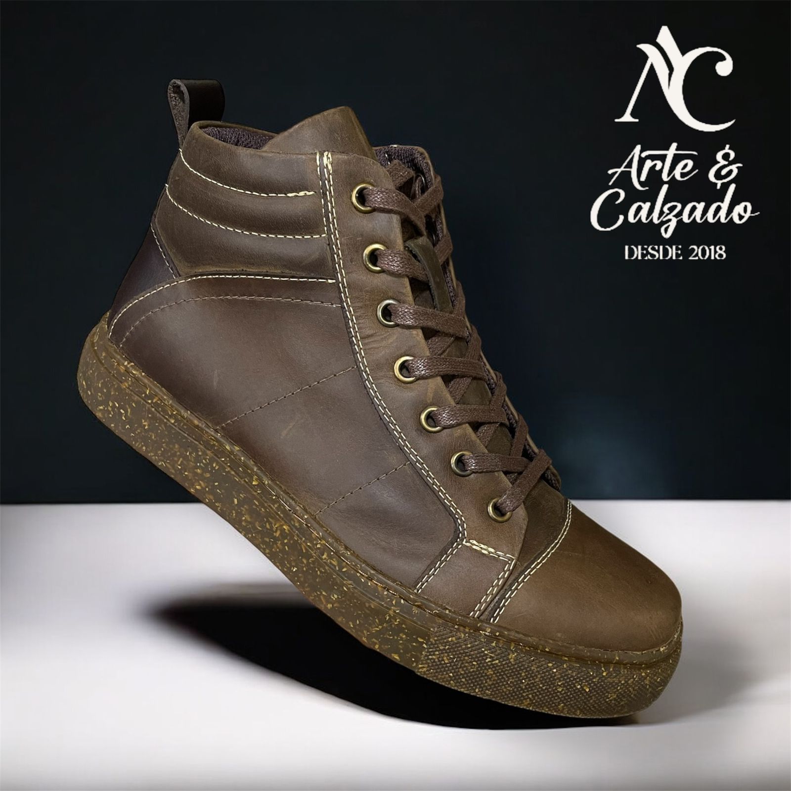 Una zapatilla deportiva alta de piel marrón con suela de goma moteada, presentada sobre un fondo blanco y negro.