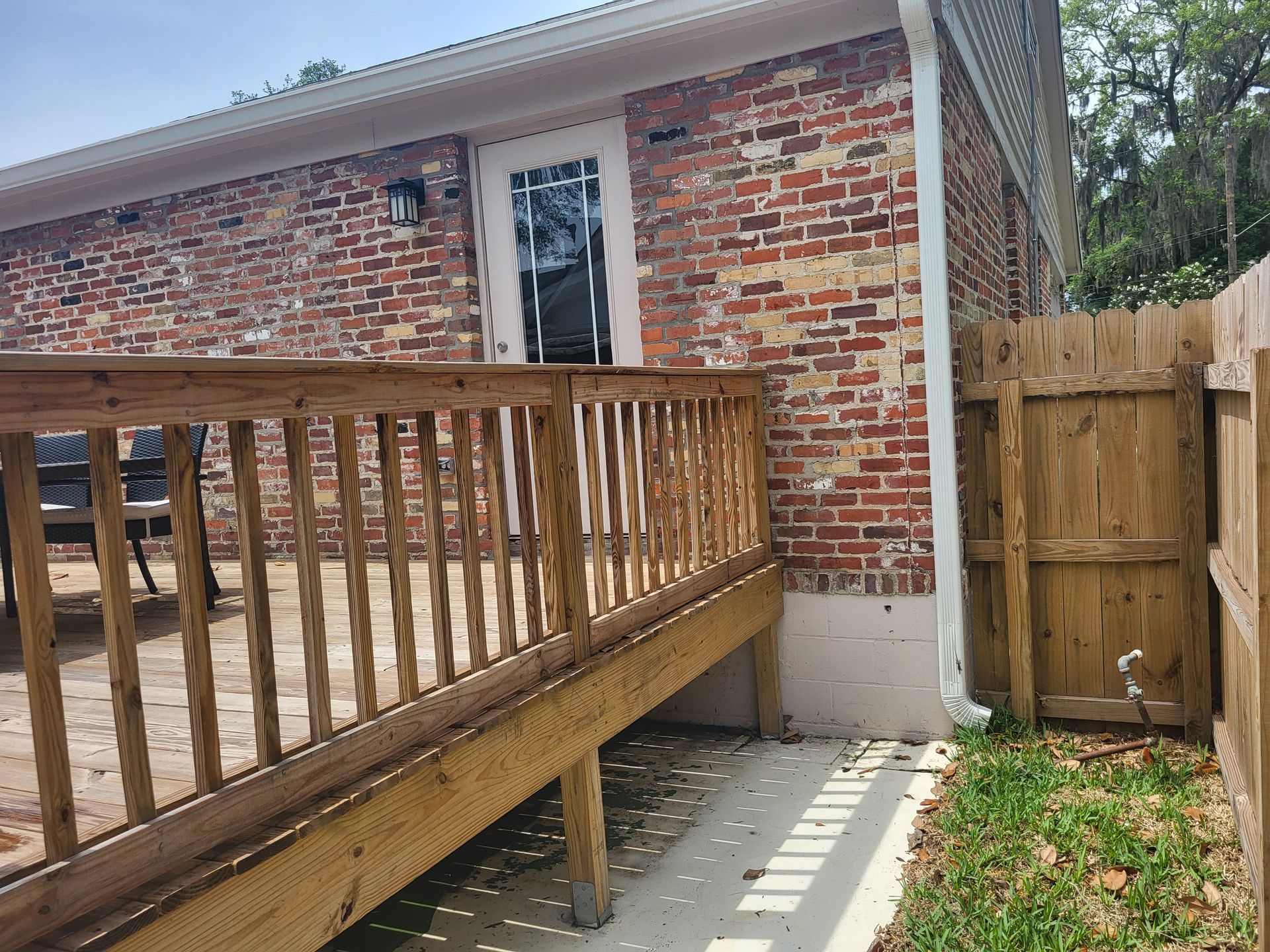Wooden deck next to a brick building and a wooden fence.