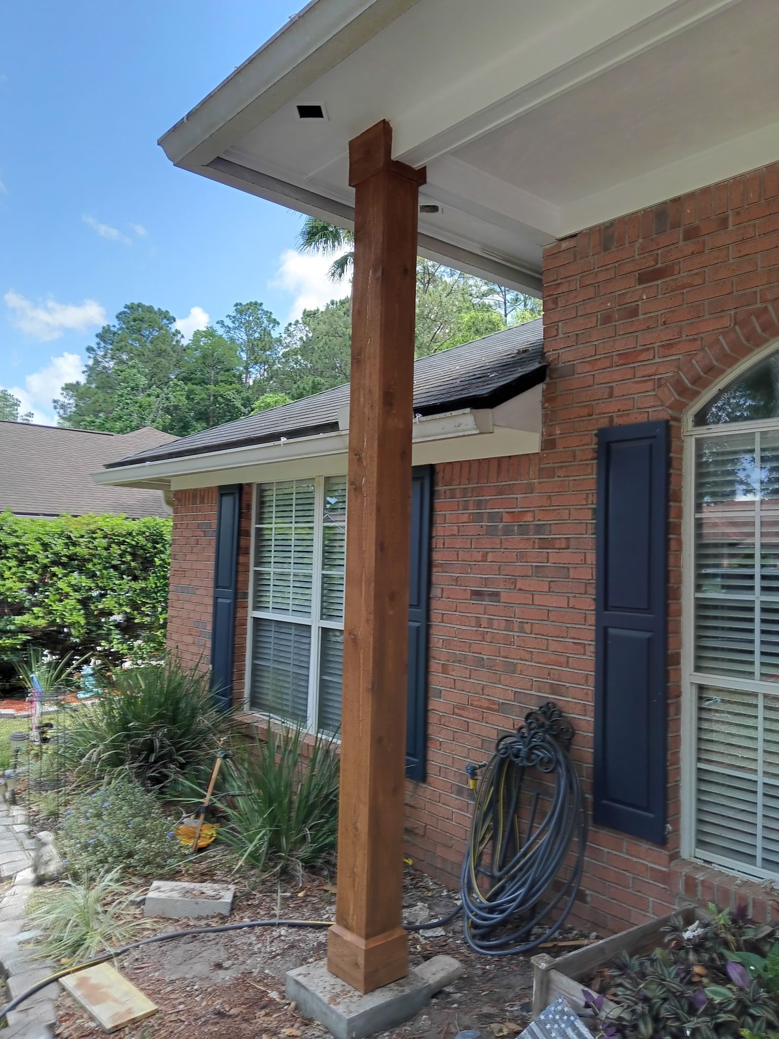 Wooden porch column supporting a white overhang on a brick house. Blue sky in the background.