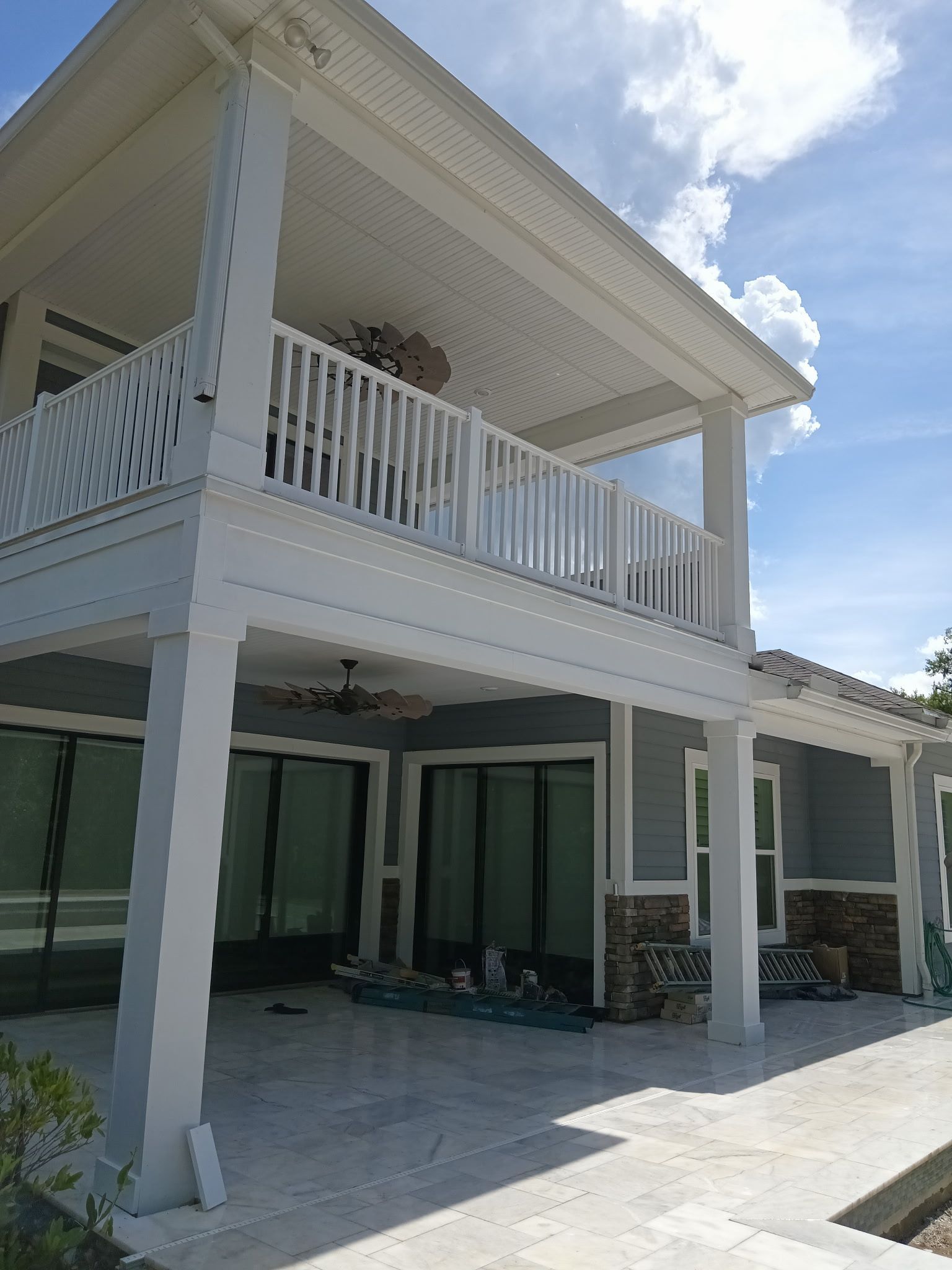 Two-story house with white railings and columns, light blue siding, and a concrete patio.