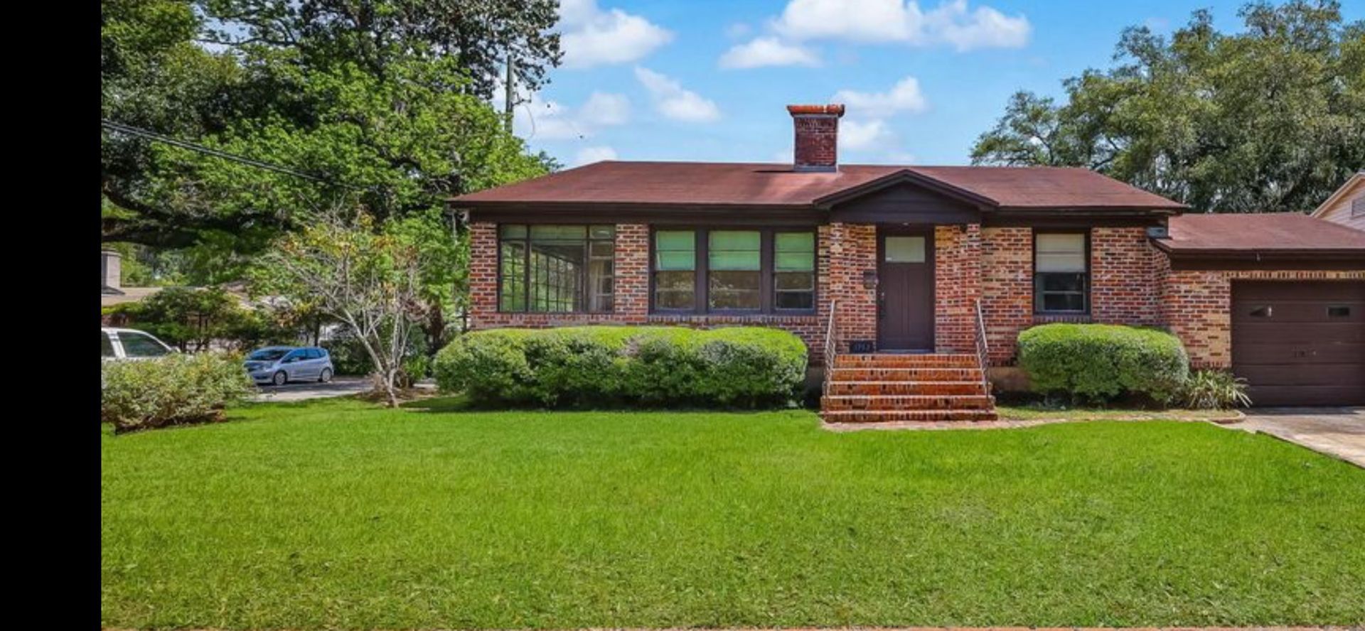 Brick house with a red roof, green lawn, and garage on a sunny day.