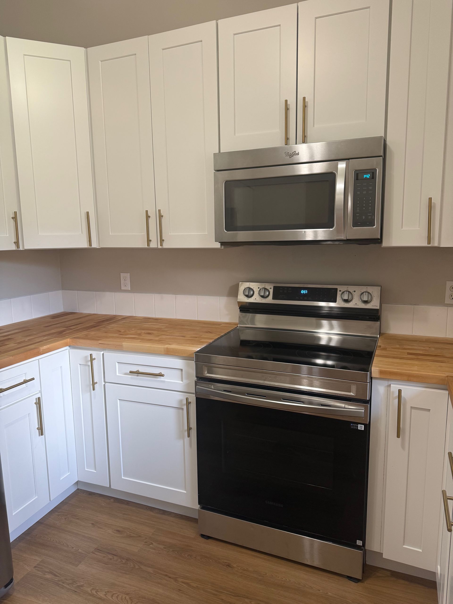 White kitchen cabinets with stainless steel appliances and wood countertops.