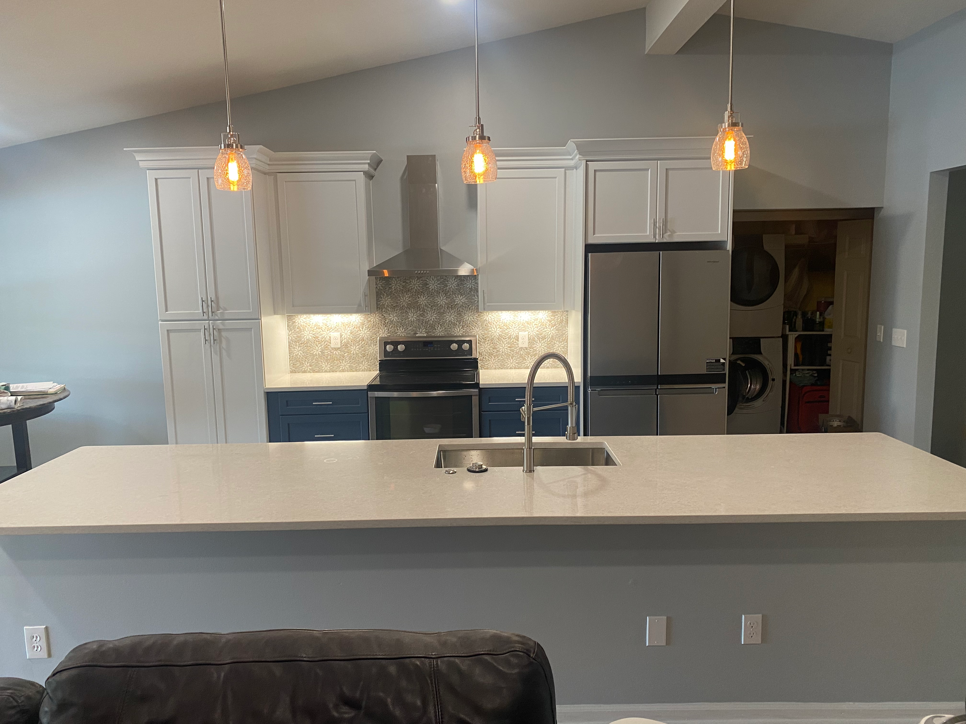 Modern kitchen with island, stainless steel appliances, white and blue cabinets, pendant lights.
