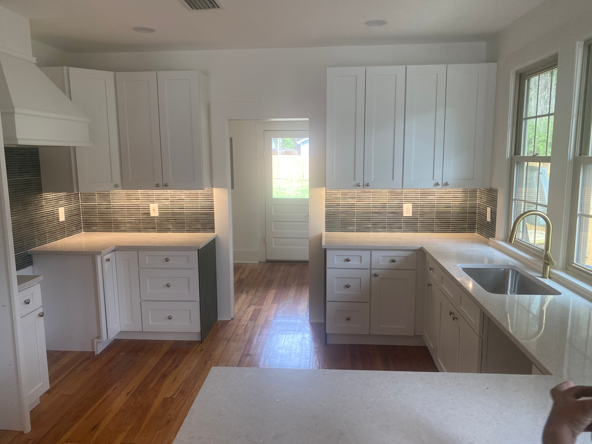 White kitchen with cabinets, backsplash, and sink, natural light from windows and door.