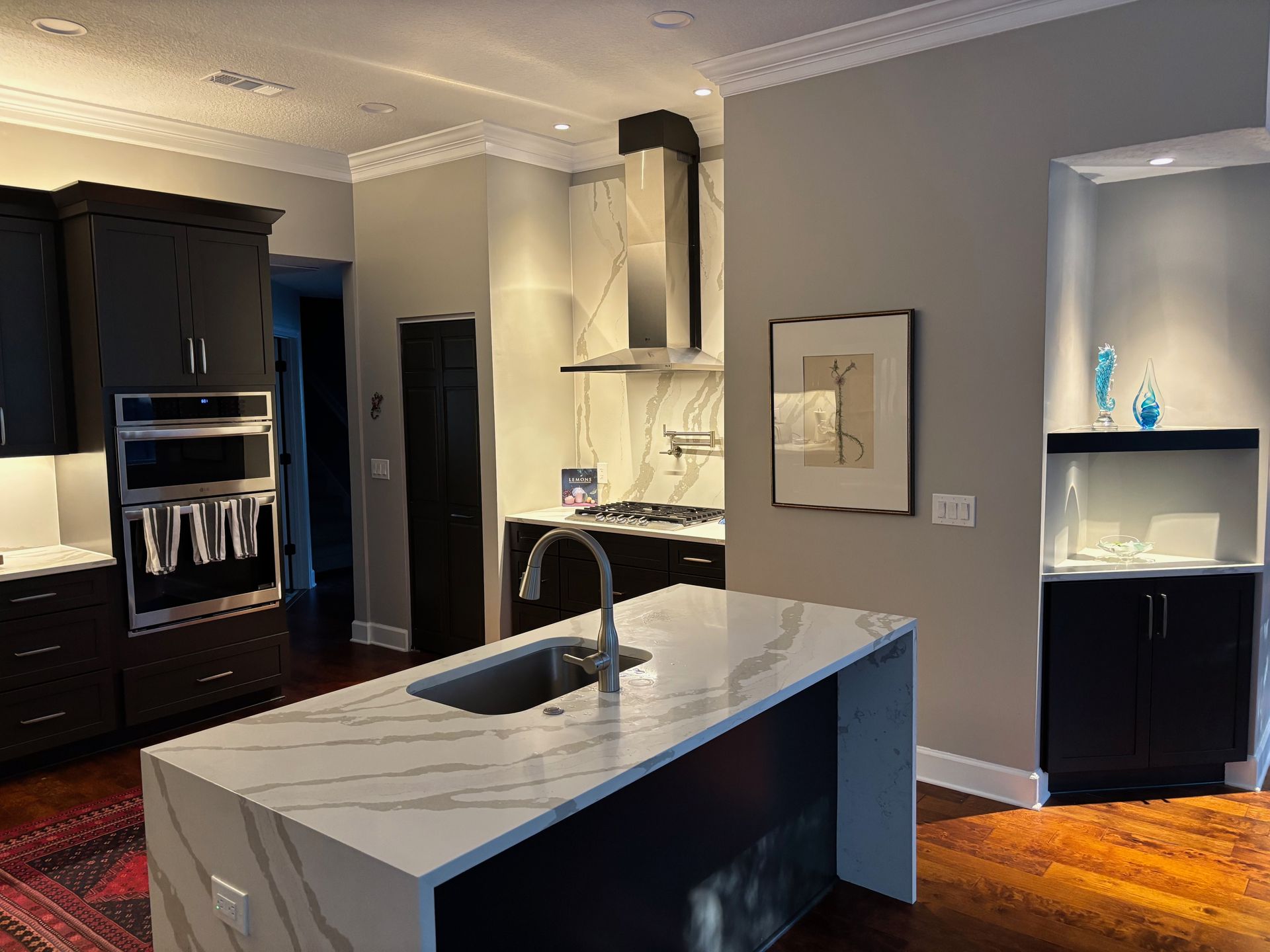 Modern kitchen with island, black cabinets, white countertops, stainless steel appliances, and a recessed art niche.