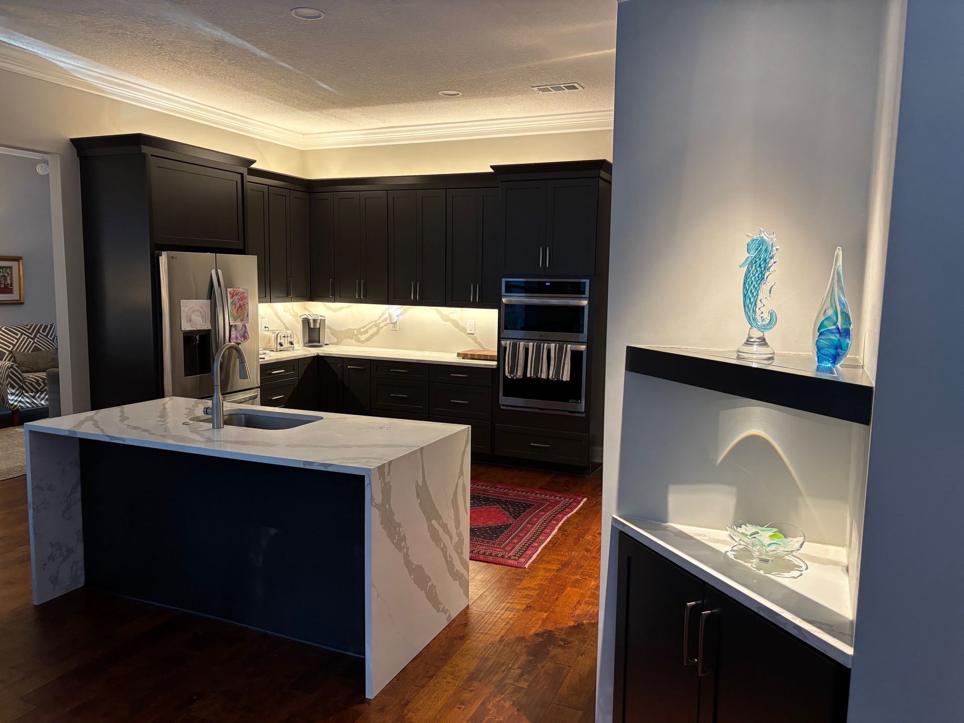 Modern kitchen with dark cabinets, white countertops, island, and decorative glass sculptures.