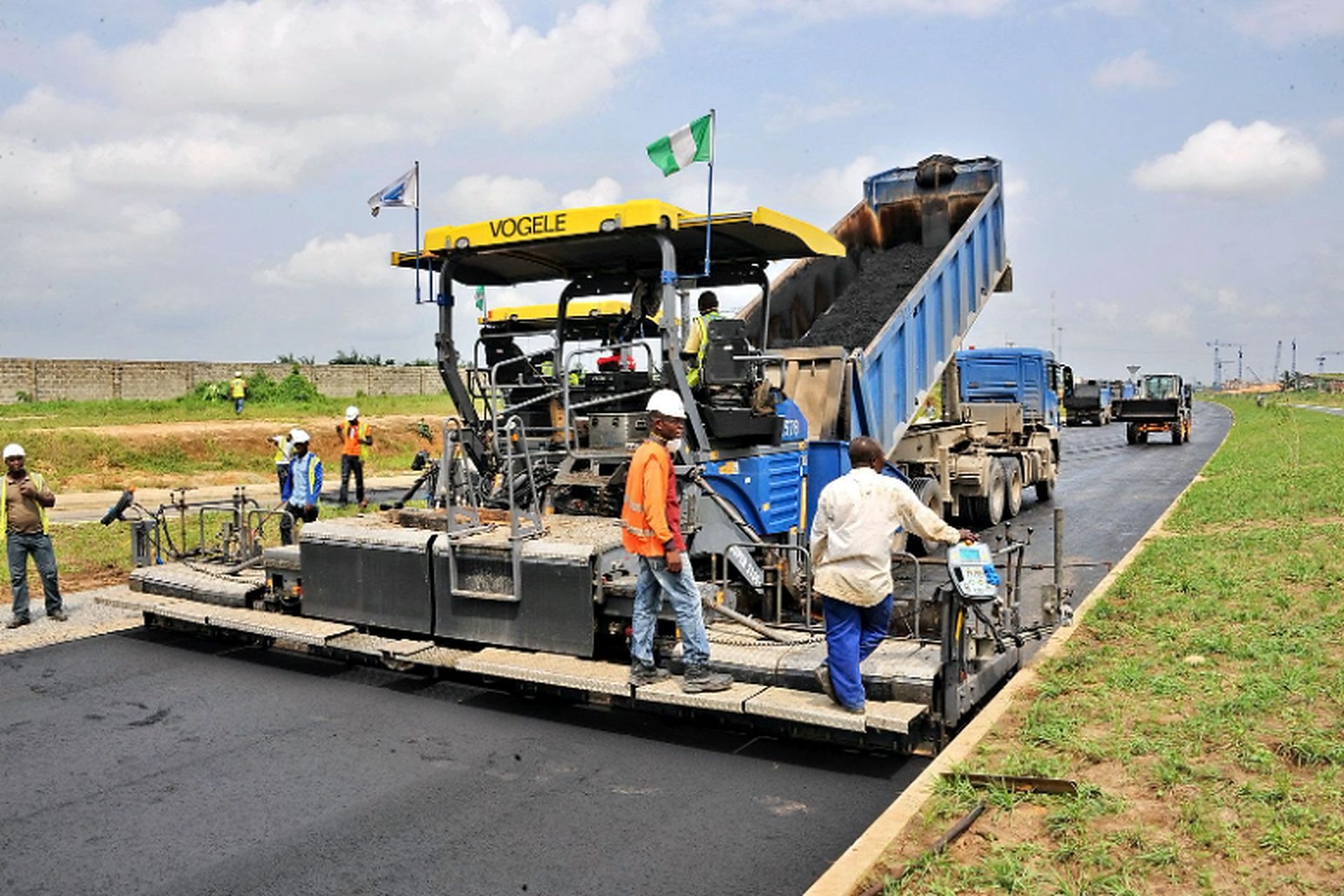 An asphalt paver and crew resurface a long road during Asphalt Paving Services in College Station, TX under clear skies.