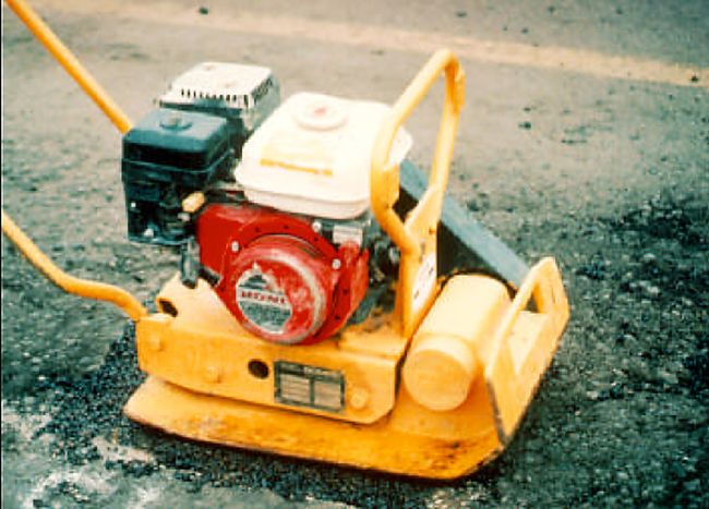 Large vibrating plate compactor sits on loose asphalt during Asphalt Paving Services in College Station, TX repair work.
