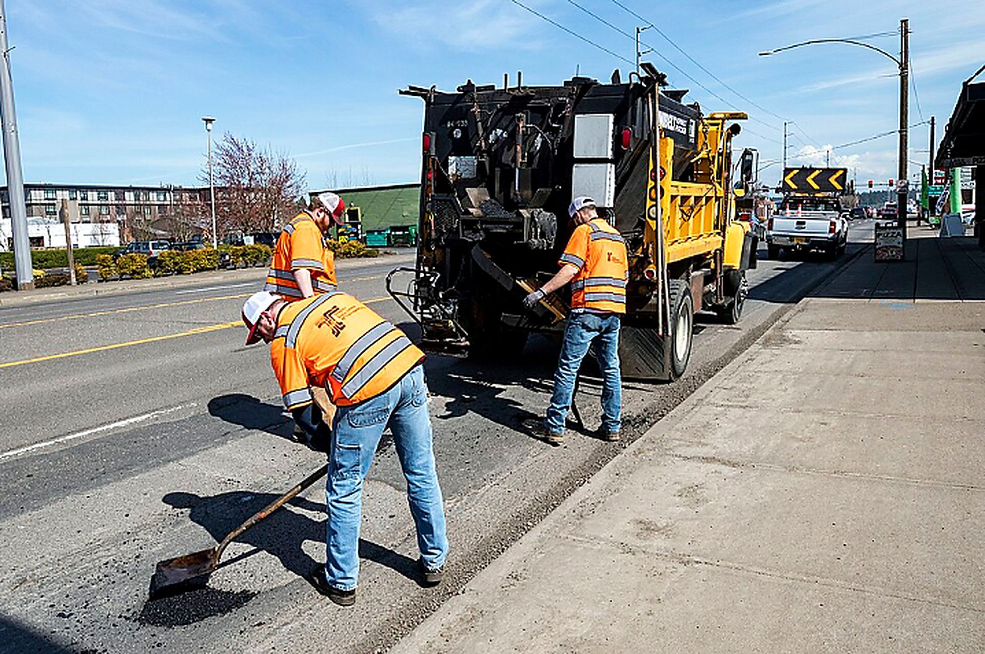 Worker rakes black asphalt beside a paving truck during Asphalt Paving Services in College Station, TX for road repairs.