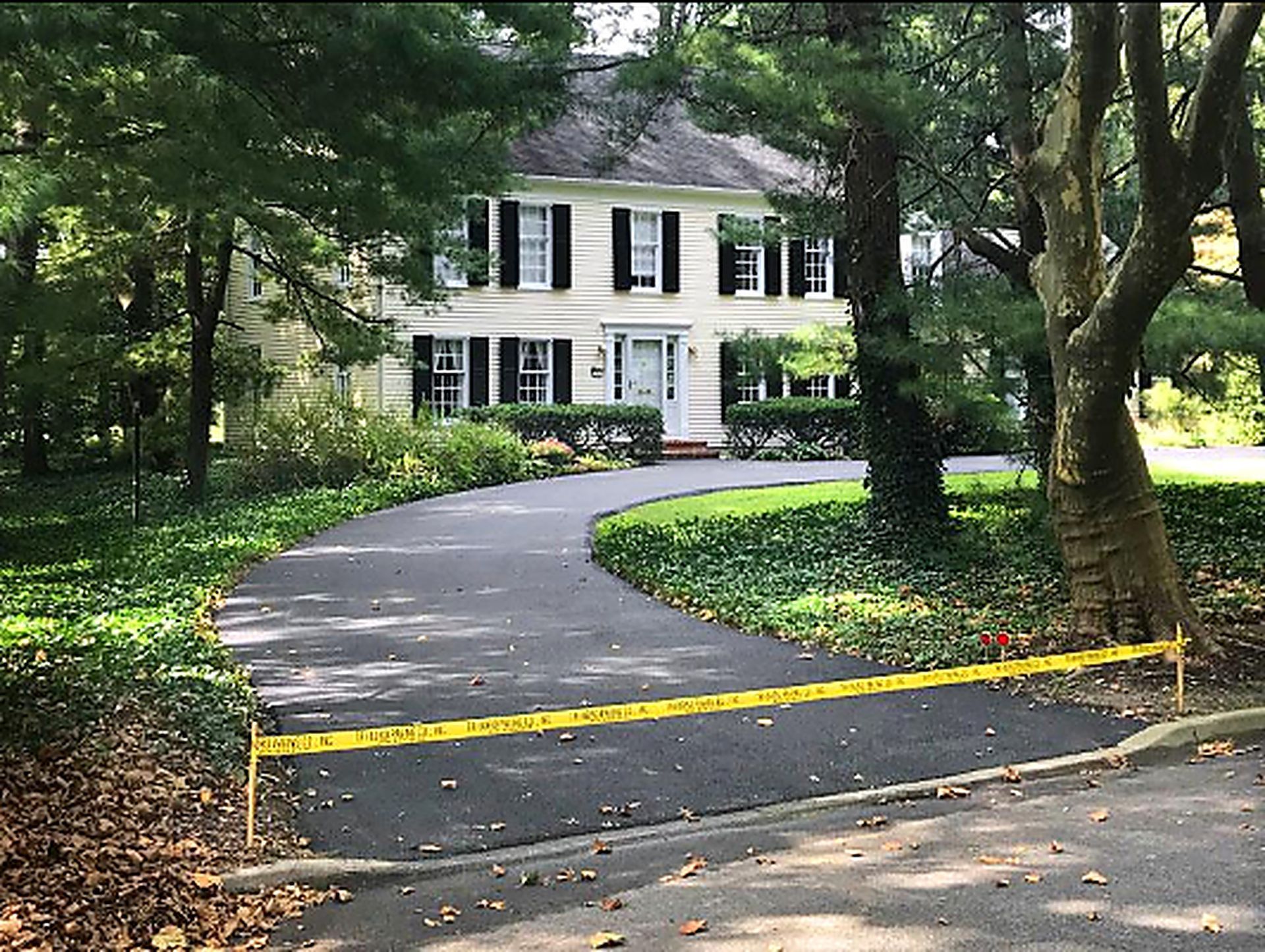 Smooth asphalt driveway curves toward a white house after Asphalt Paving Services in College Station, TX by green trees.