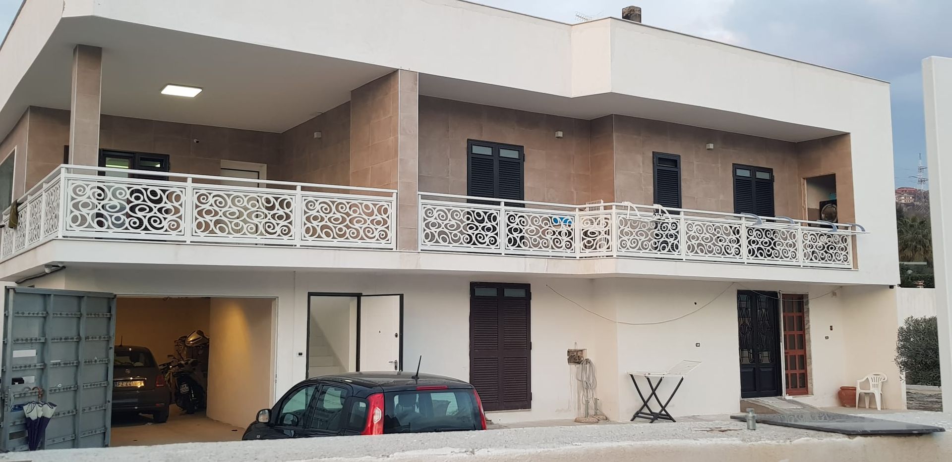 Casa beige a due piani con ringhiere del balcone bianche, garage e auto parcheggiate davanti.