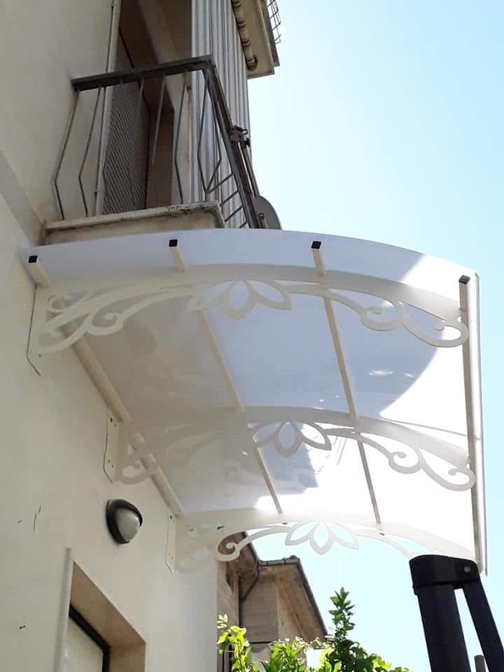 Tenda da sole curva bianca con staffe laterali decorative a motivi floreali, montata sopra una porta di un edificio di colore chiaro.