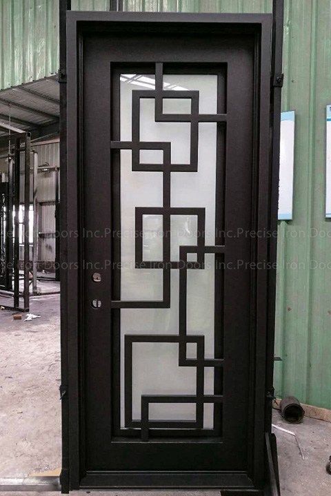 Una porta esterna in metallo nero con un motivo geometrico a quadrati su un inserto in vetro satinato, inserita in un'officina industriale.