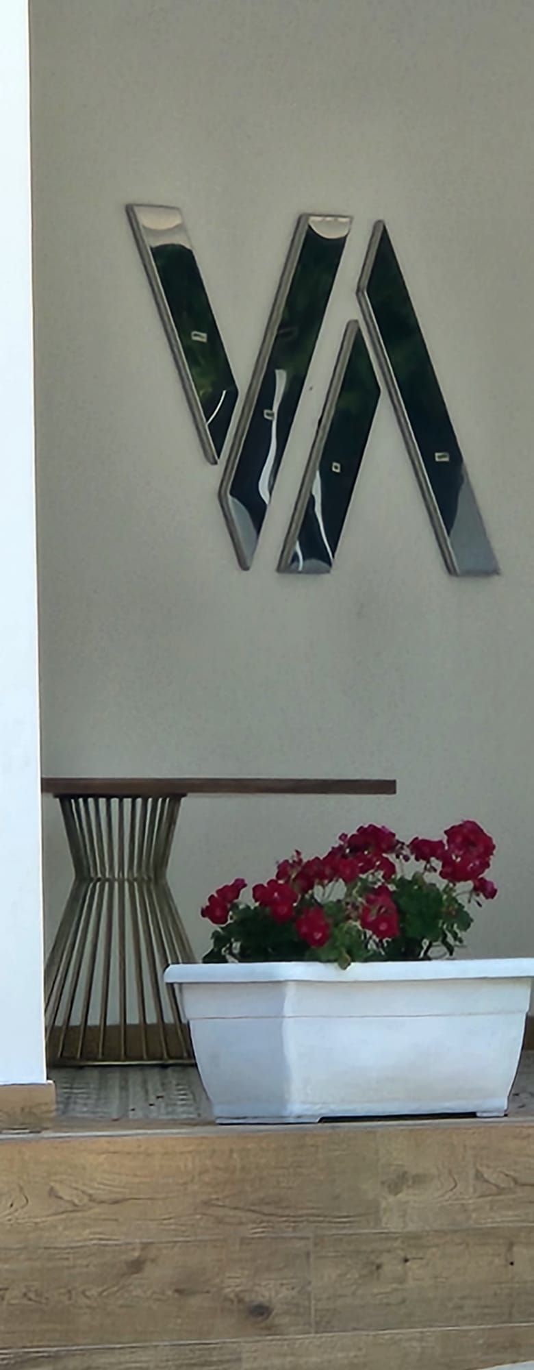 Decorazione murale moderna con una fioriera bianca di fiori rossi accanto a un supporto intrecciato su una parete chiara.