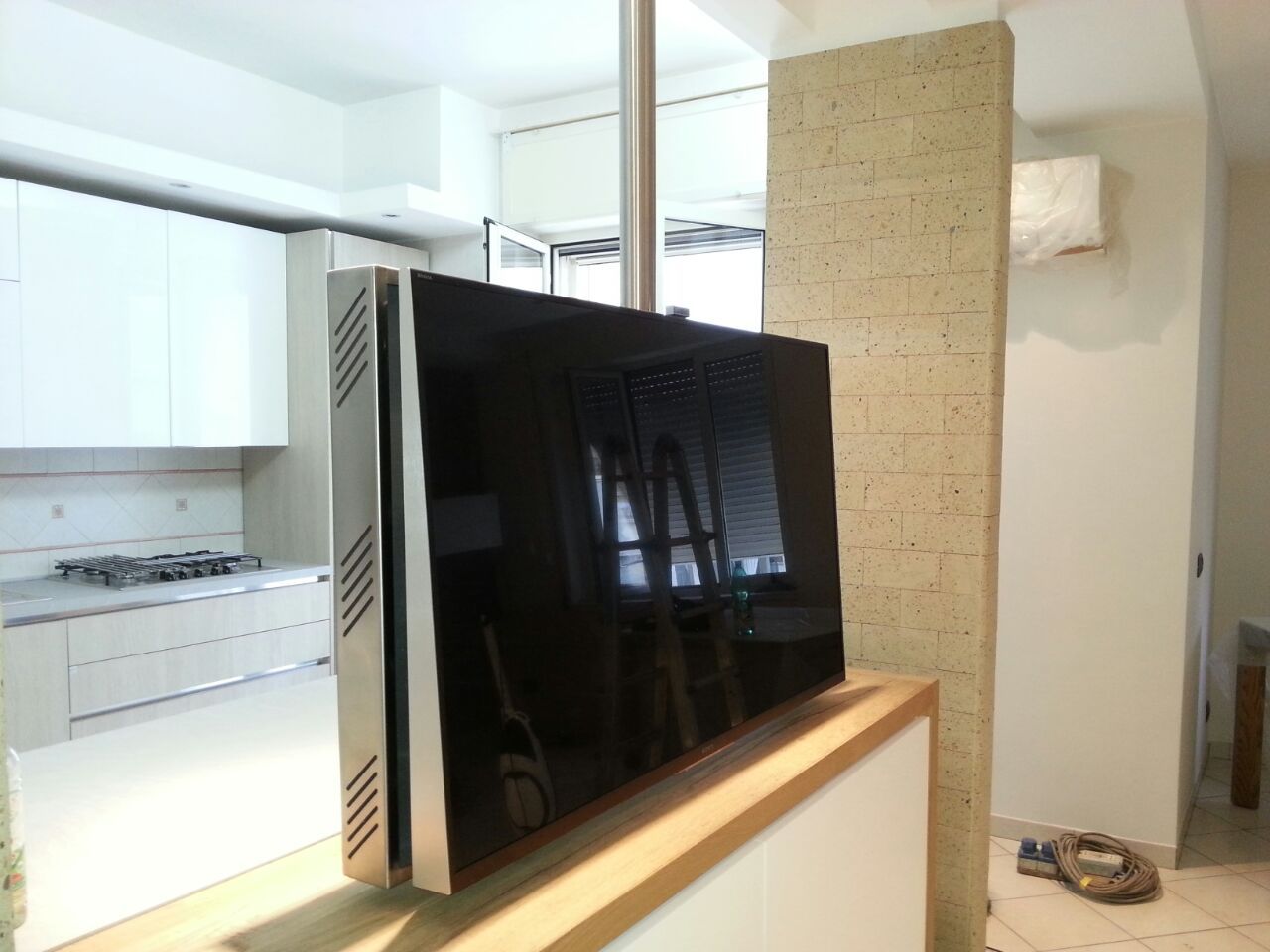Ampio televisore a schermo piatto montato su un supporto in una luminosa cucina moderna.