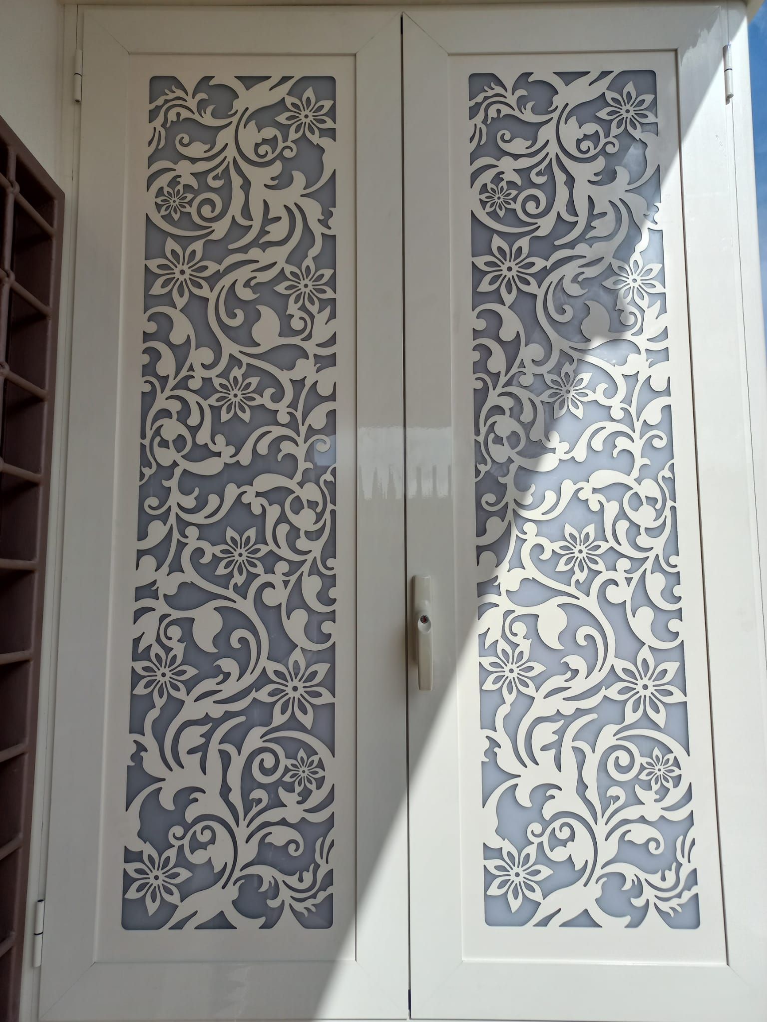 Ante doppie bianche per mobiletto con pannelli floreali decorati e maniglia centrale.