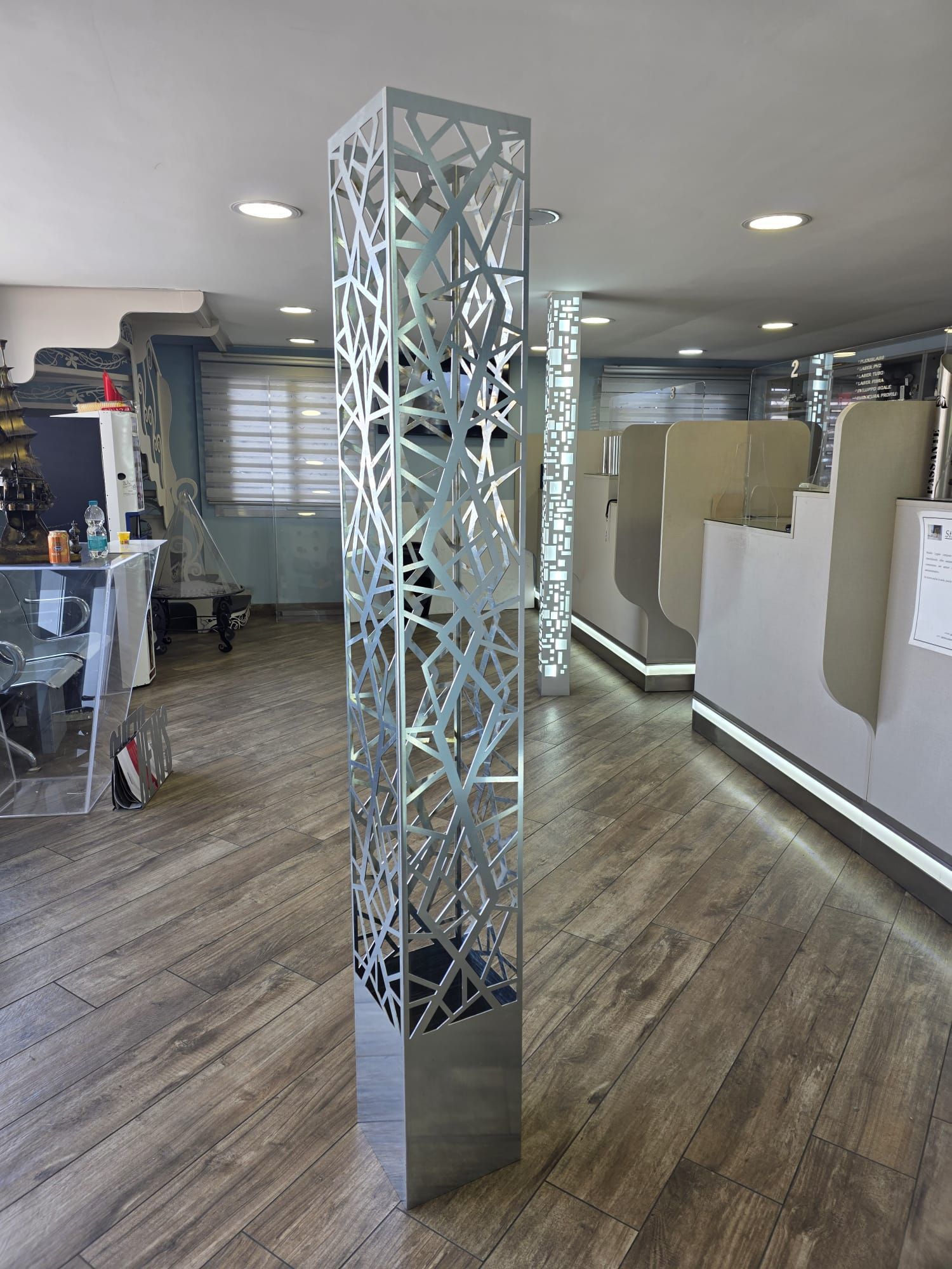 Scultura geometrica argentata da pavimento in uno showroom moderno con pavimento in legno e faretti a incasso a soffitto.