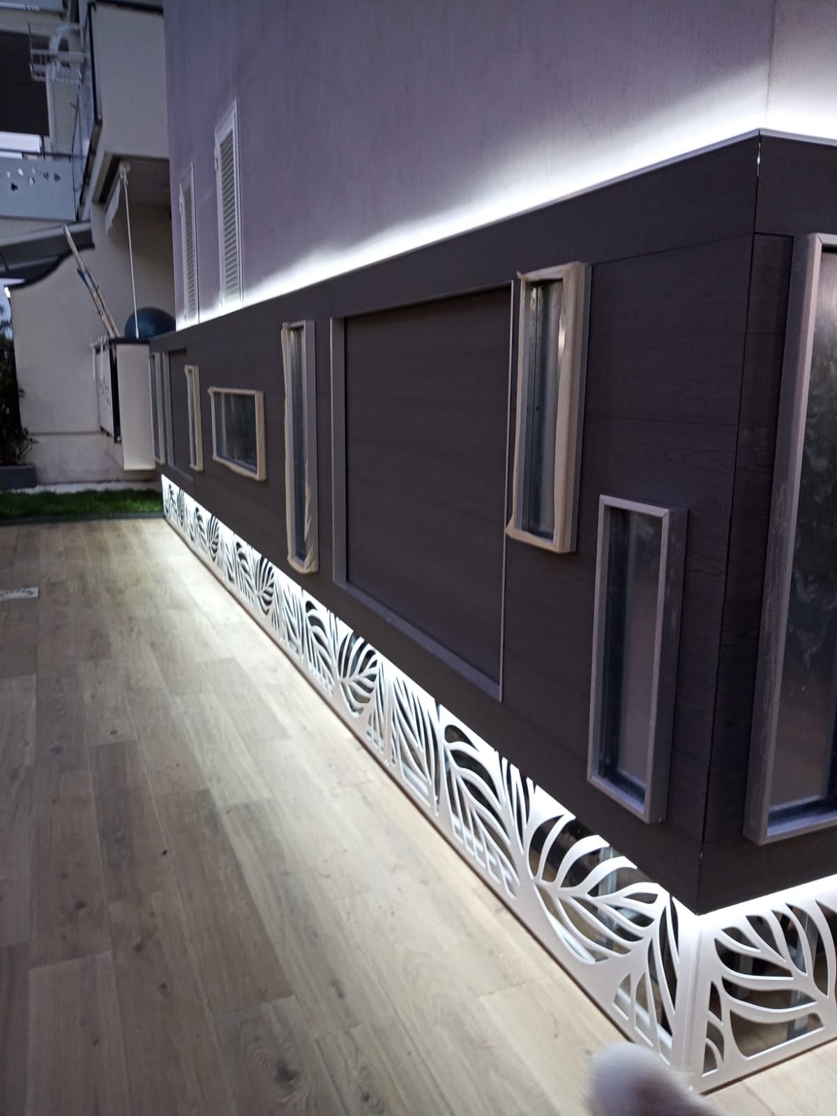 Patio interno moderno con pannelli a parete scuri, piccole finestre e un battiscopa bianco decorato con pavimento in legno