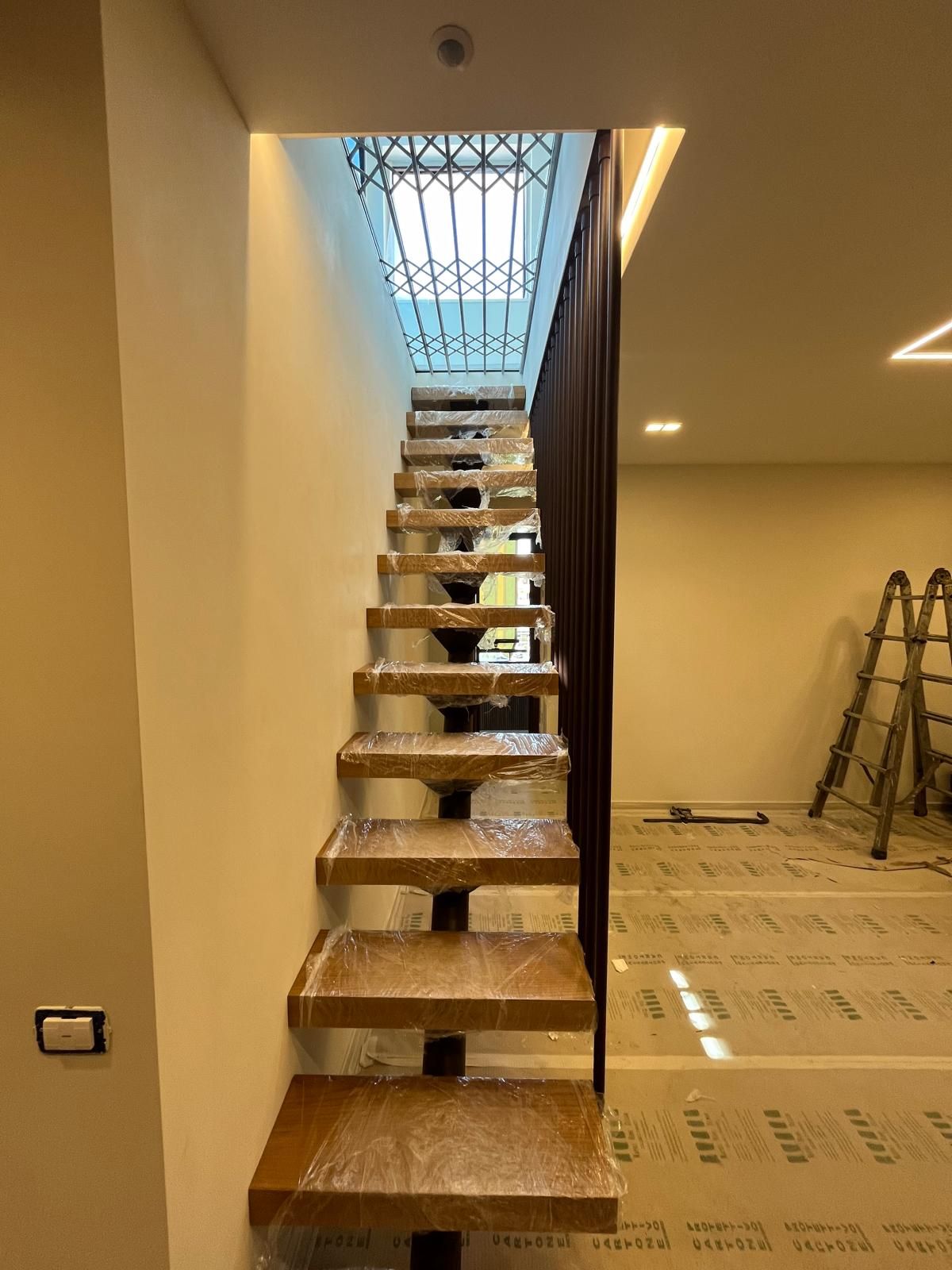 Scala interna con gradini in legno a vista che conduce a un pianerottolo illuminato da un lucernario in uno spazio ristrutturato.