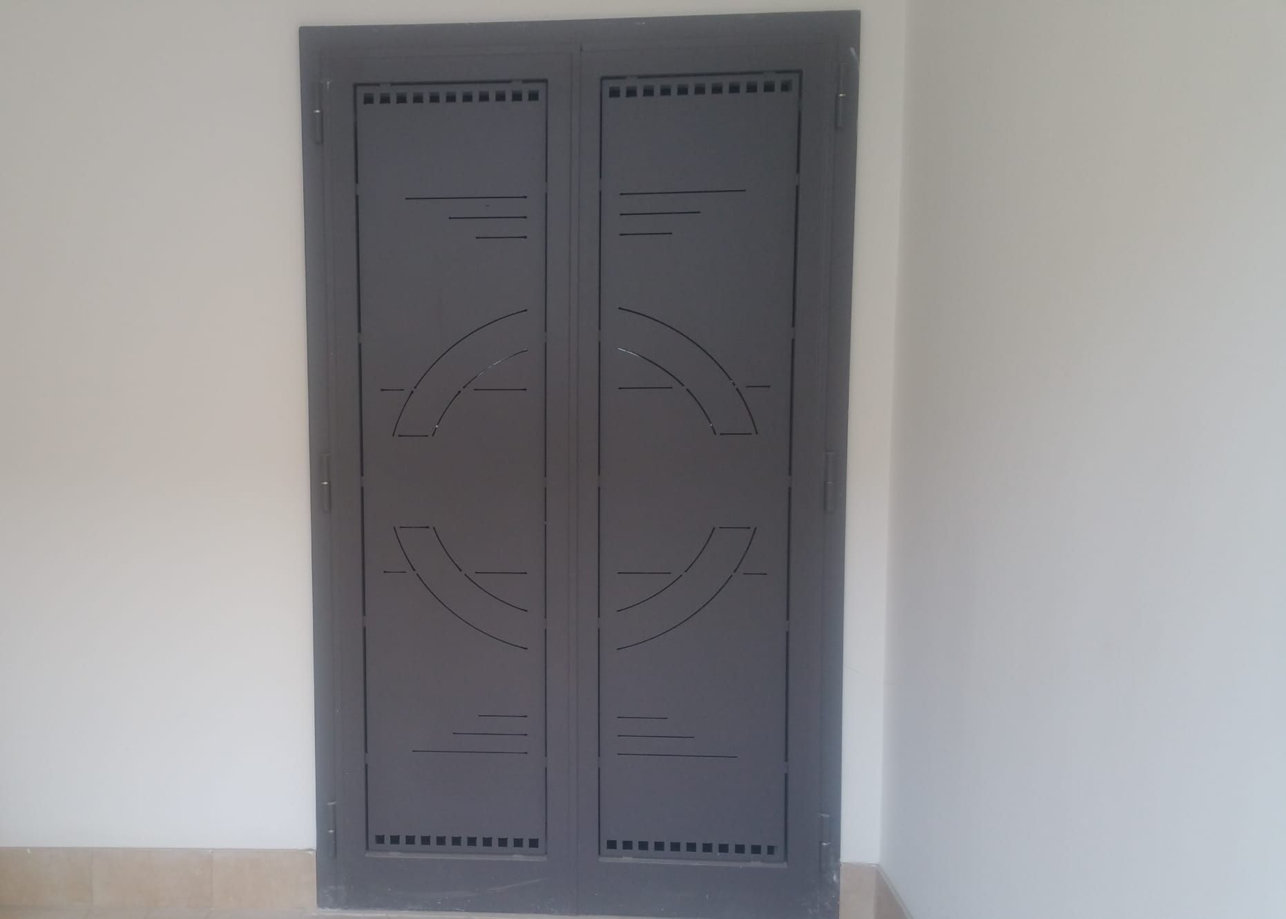Mobile doppio in metallo grigio con intagli circolari decorativi su una parete bianca