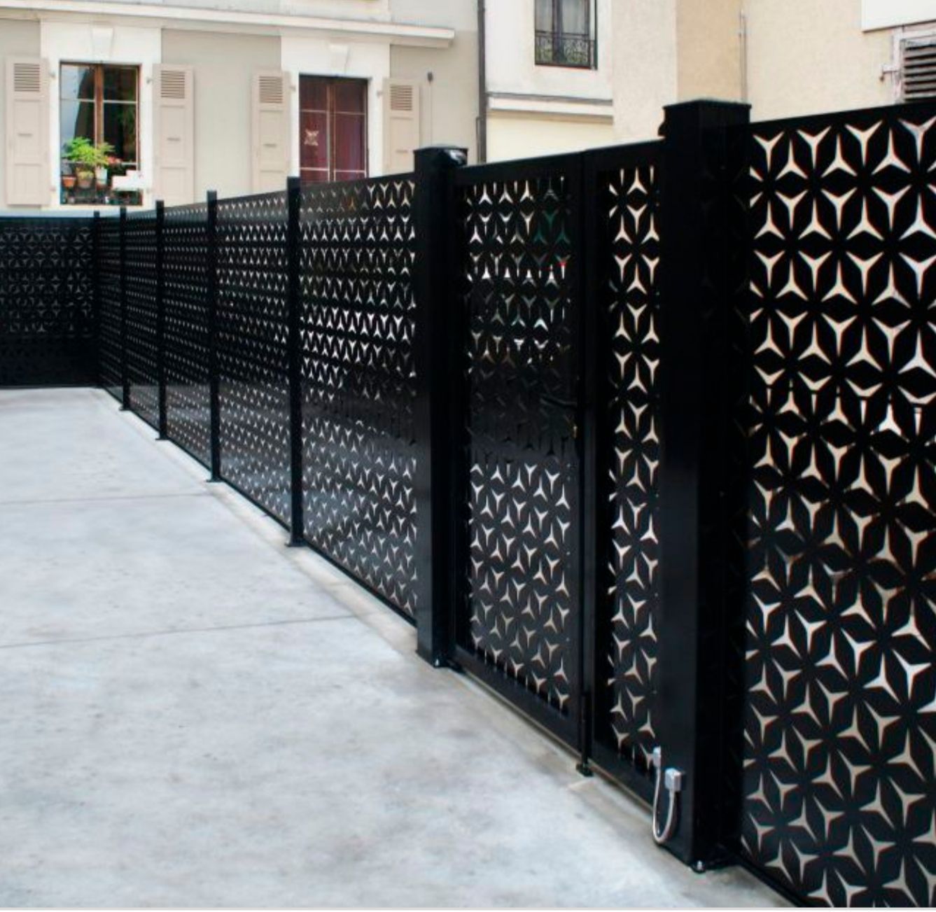 Recinzione e cancello in metallo decorativo nero lungo un vialetto in cemento accanto a una casa