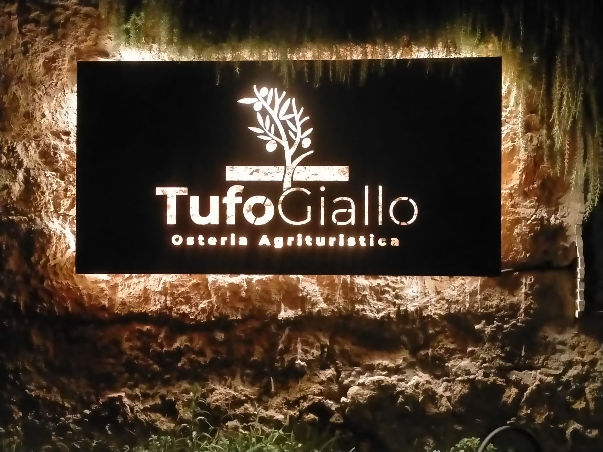 L'insegna del ristorante TufoGiallo brilla su un muro di pietra di notte.