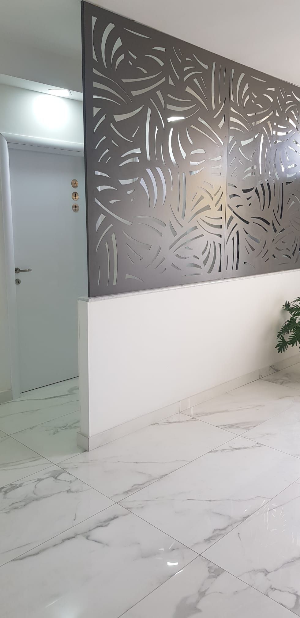 Corridoio moderno con pavimento in marmo bianco e pannello decorativo grigio a parete accanto a una porta.