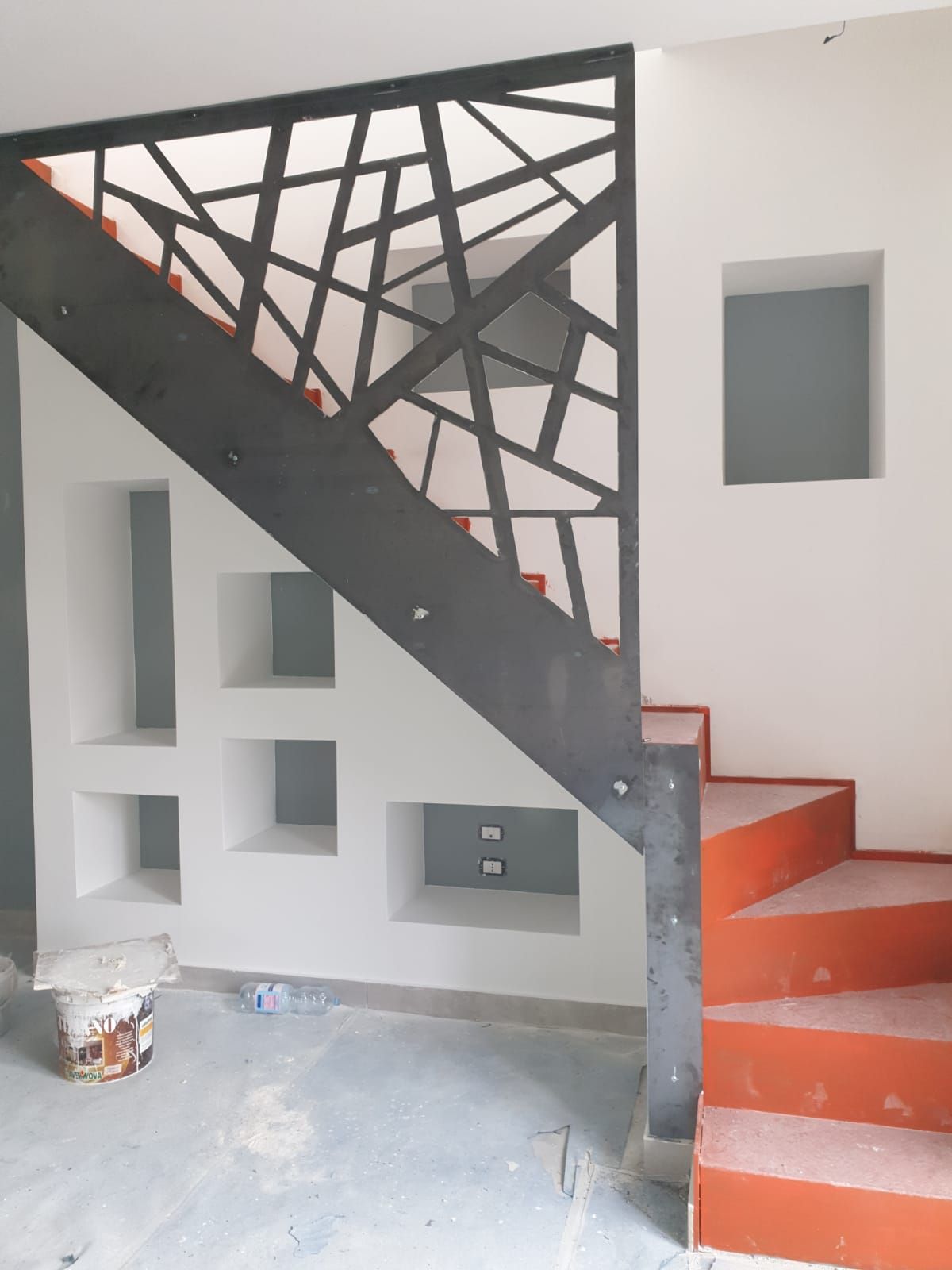 Scala interna con ringhiera nera e gradini arancioni, addossata a una parete bianca con nicchie integrate.