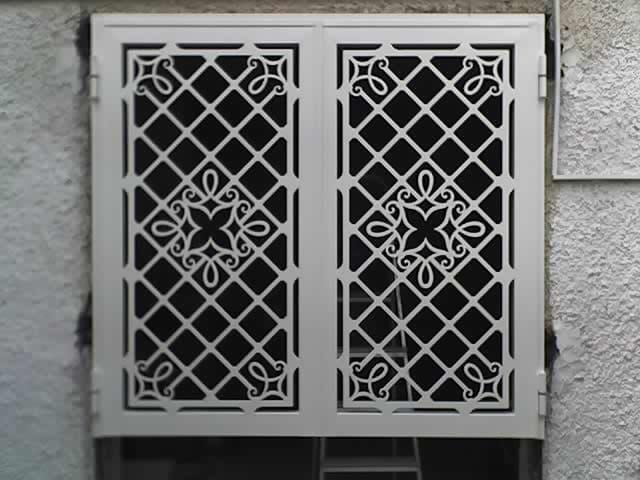 Griglia di sicurezza decorativa in metallo su una piccola finestra o presa d'aria a muro, in una parete di pietra grigia