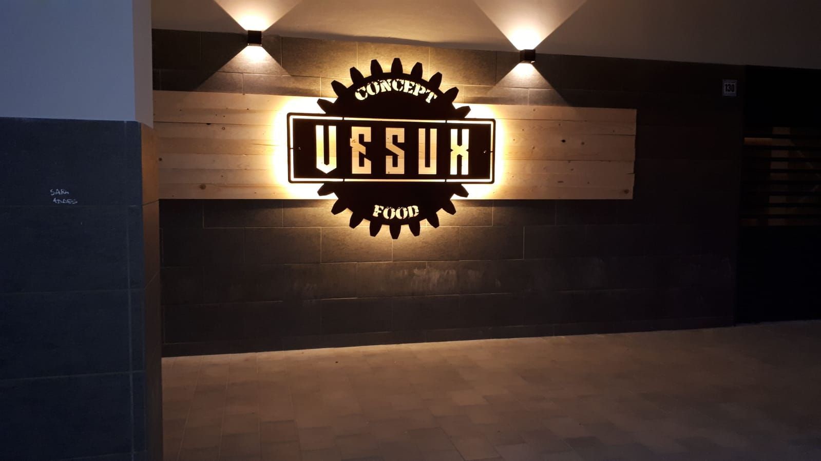 Insegna luminosa UESUH su una parete di legno sopra l'interno buio di una vetrina.