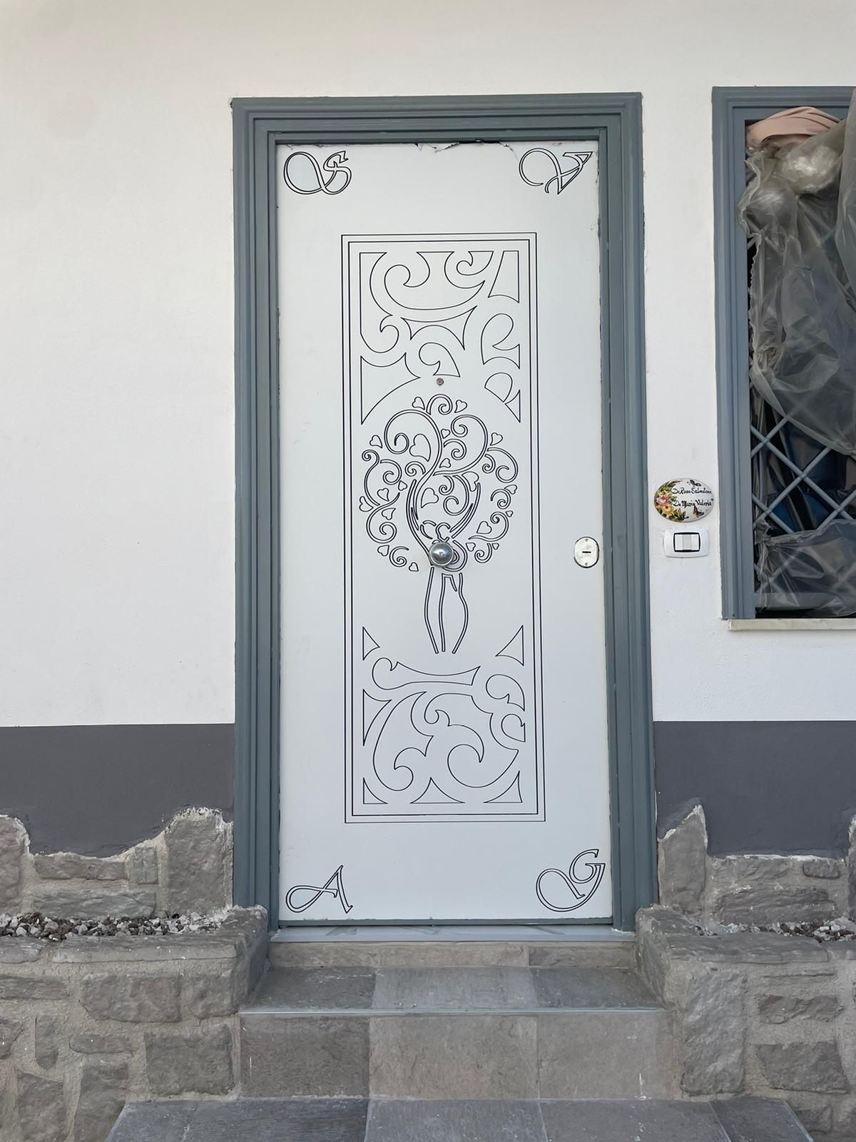 Porta d'ingresso decorativa bianca con elaborati disegni in metallo e gradini in pietra incastonati in un muro esterno grigio.