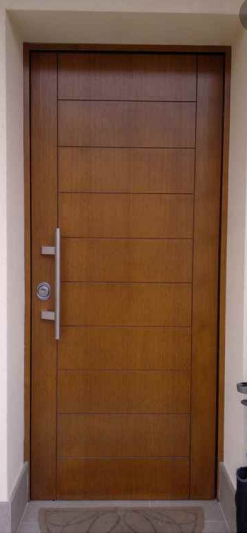 Porta d'ingresso in legno con maniglia e serratura argentate in un vano porta beige
