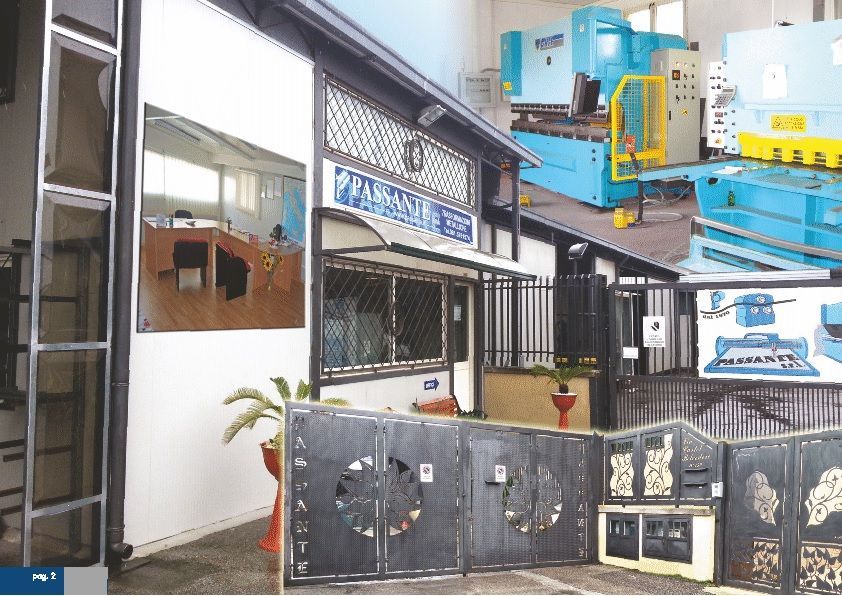 Ingresso di un'officina industriale con macchinari blu all'interno e cancello metallico nero all'esterno.