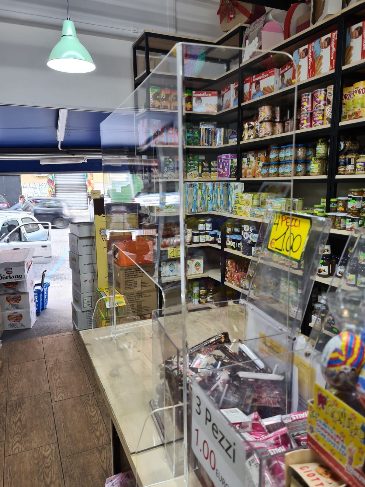 Corridoio di un piccolo minimarket con vetrine, scaffali di snack e una luce verde sospesa vicino all'ingresso.